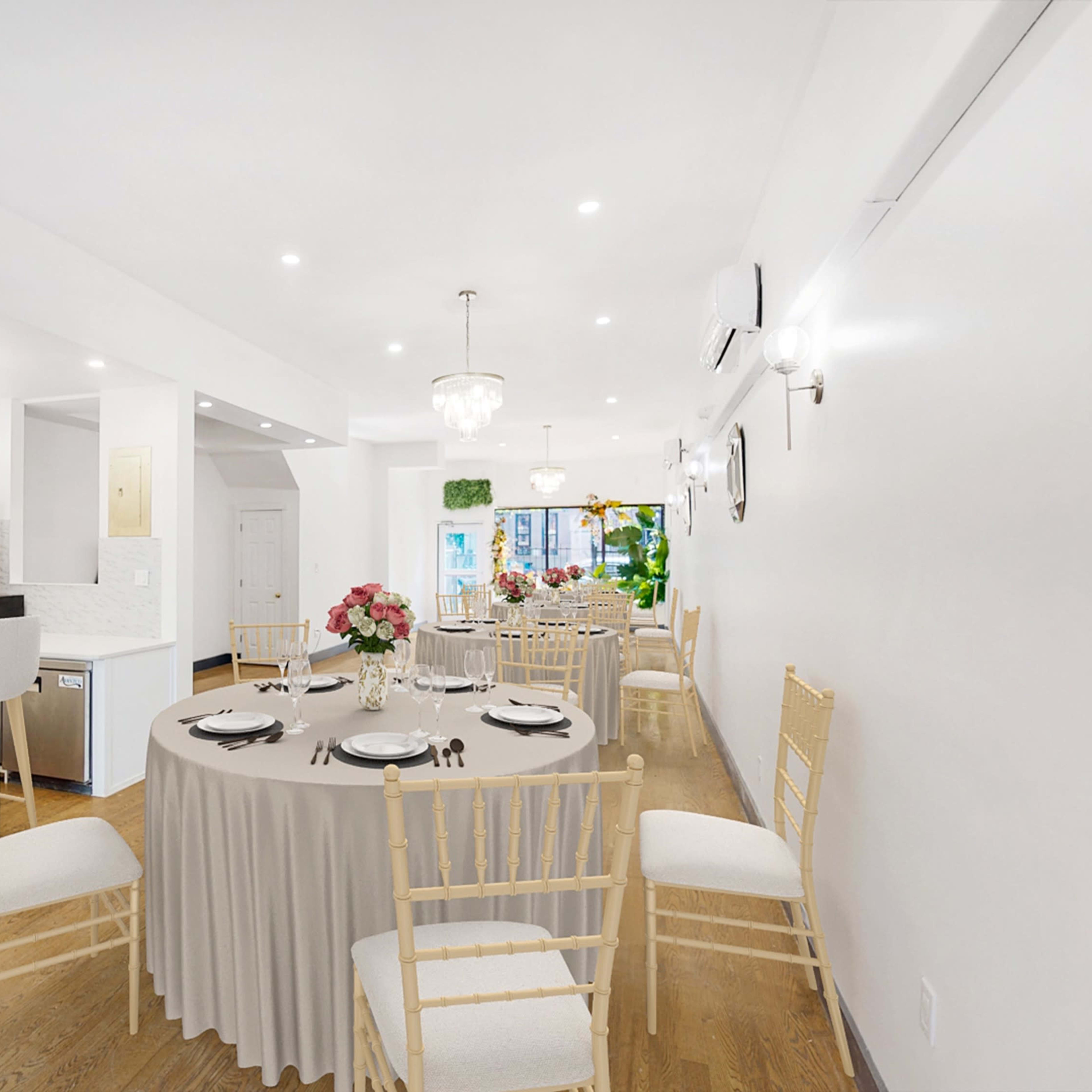 A dining area set with a round table and chairs, featuring floral centerpieces and a modern kitchen in the background.