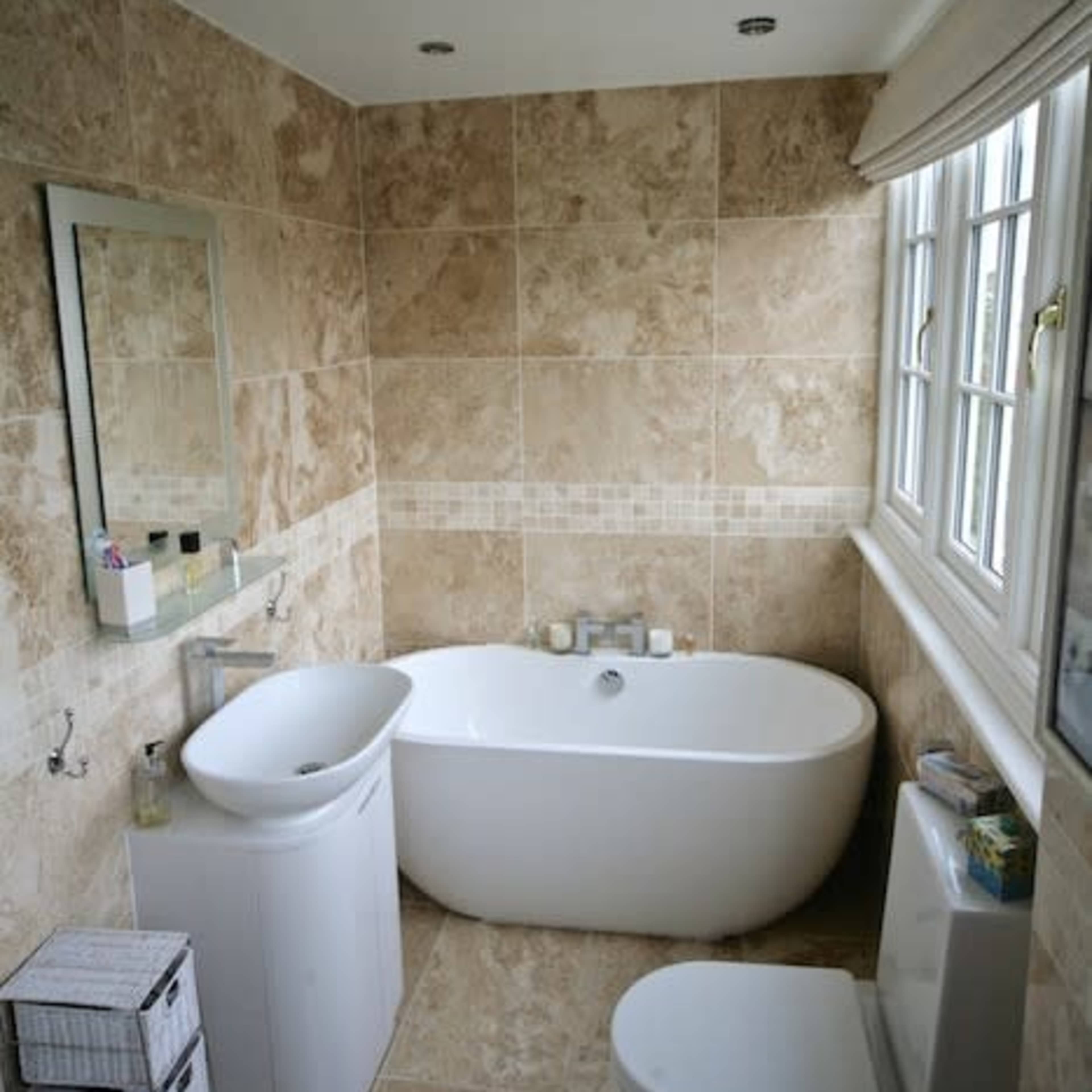 A bathroom with stone-tiled walls, a freestanding bathtub, a modern sink, and a toilet.
