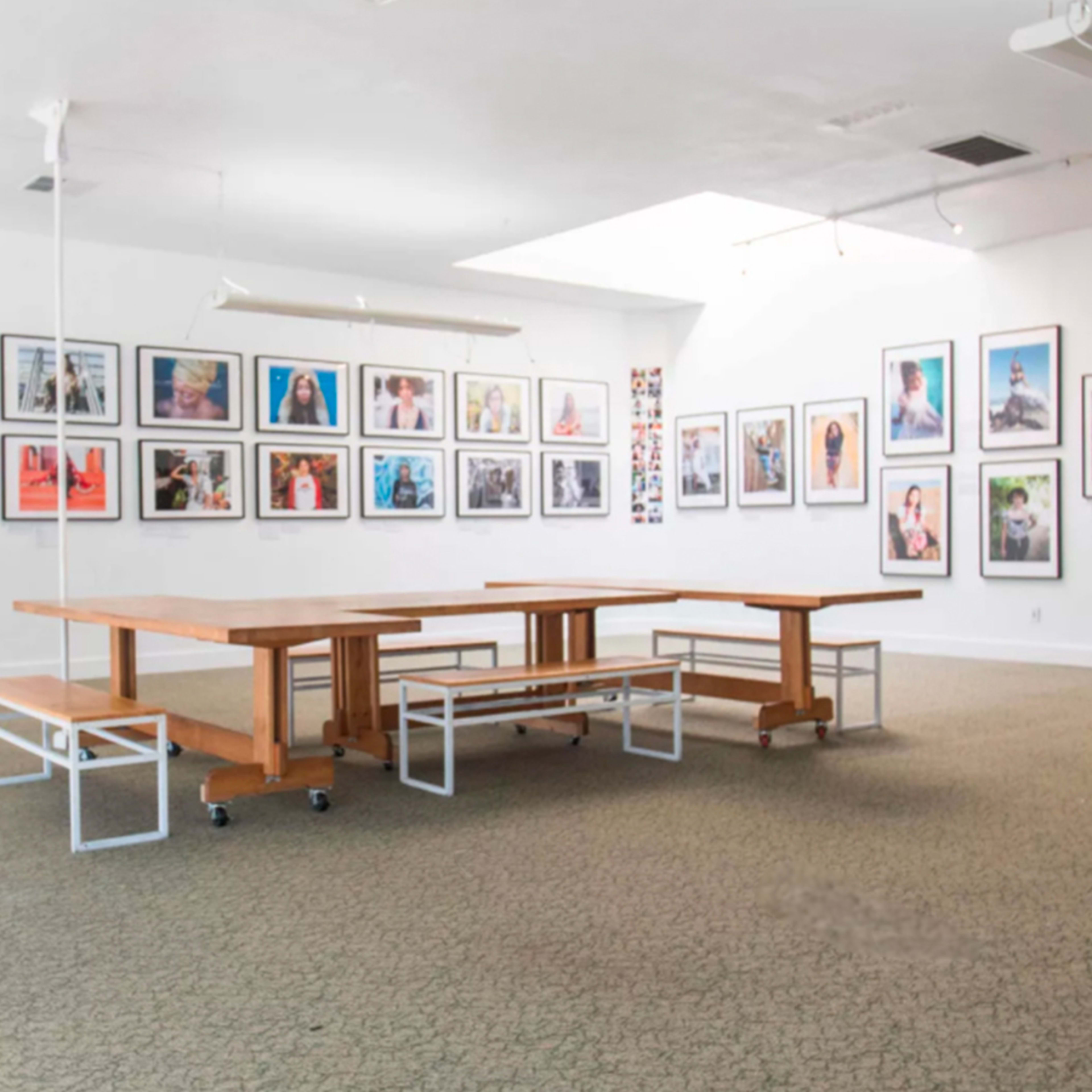 A spacious gallery with several framed photographs displayed on the walls and a large wooden table surrounded by benches in the center.