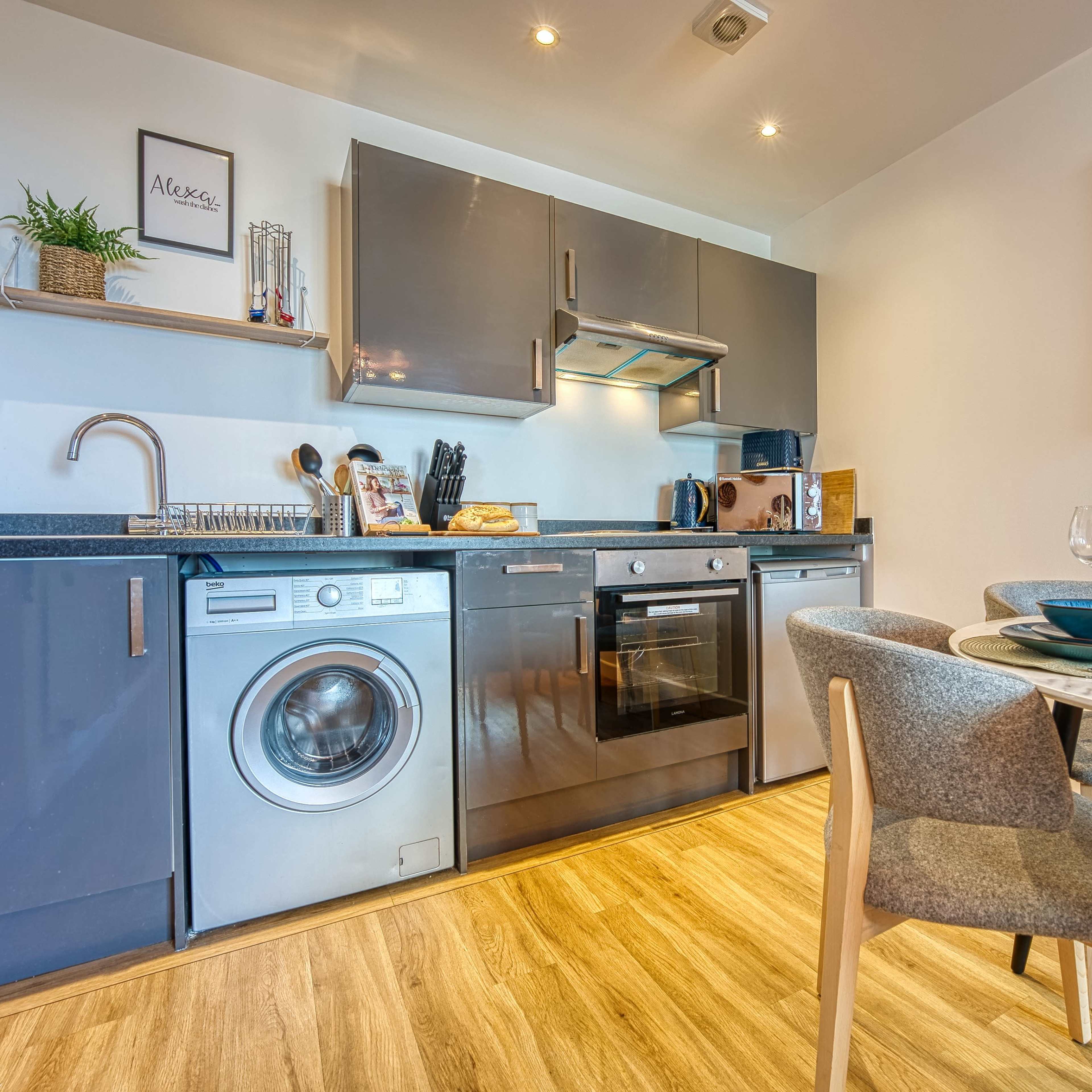 A modern kitchen with stainless steel appliances, a washing machine, and a dining table set for two.