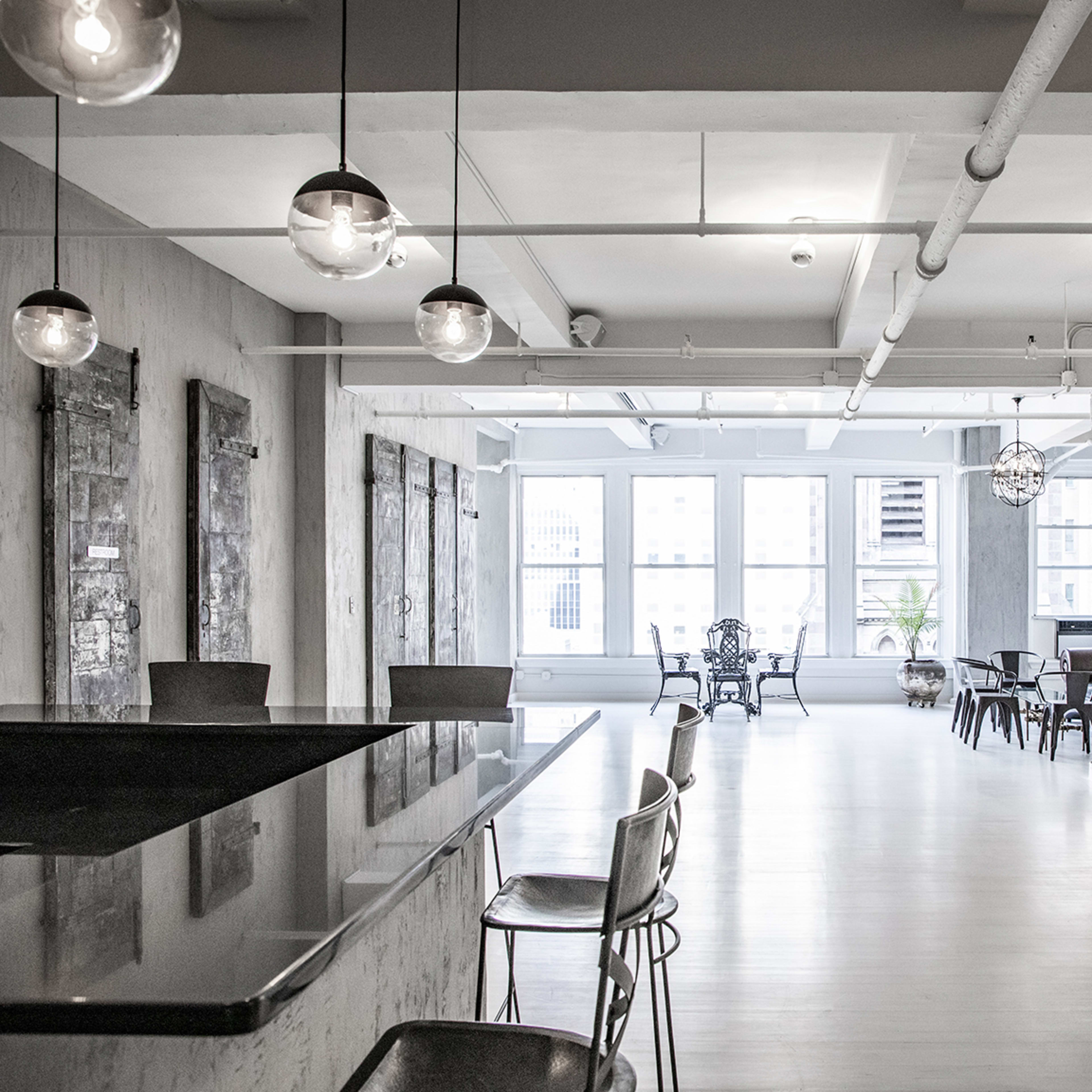 A spacious, modern room with a minimalist design, featuring large windows, a bar counter, and various seating arrangements.