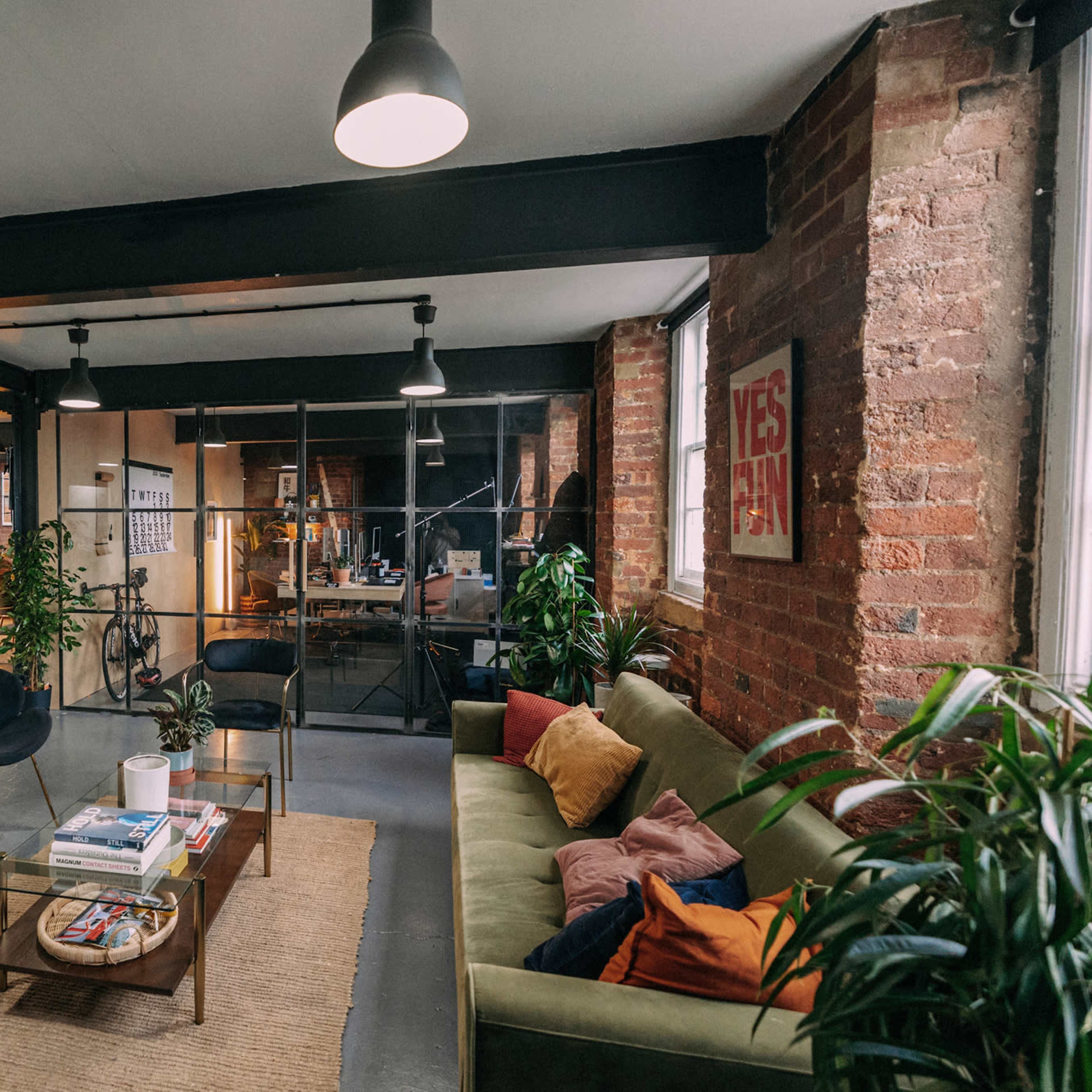 A stylish office space with exposed brick walls, modern furniture, and a cozy seating area surrounded by plants.