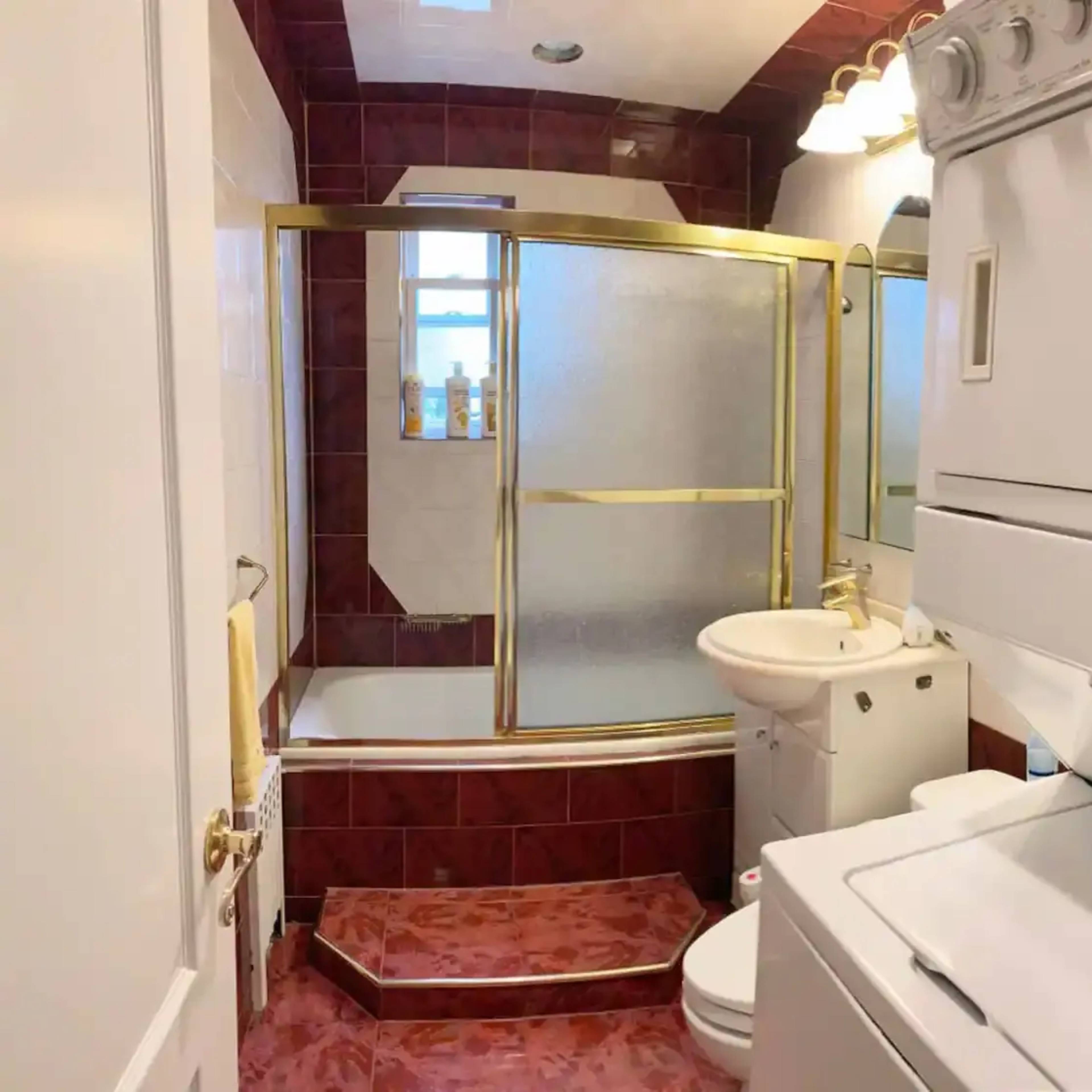 A compact bathroom featuring a shower with a glass door, a toilet, a sink, and stacked laundry appliances.