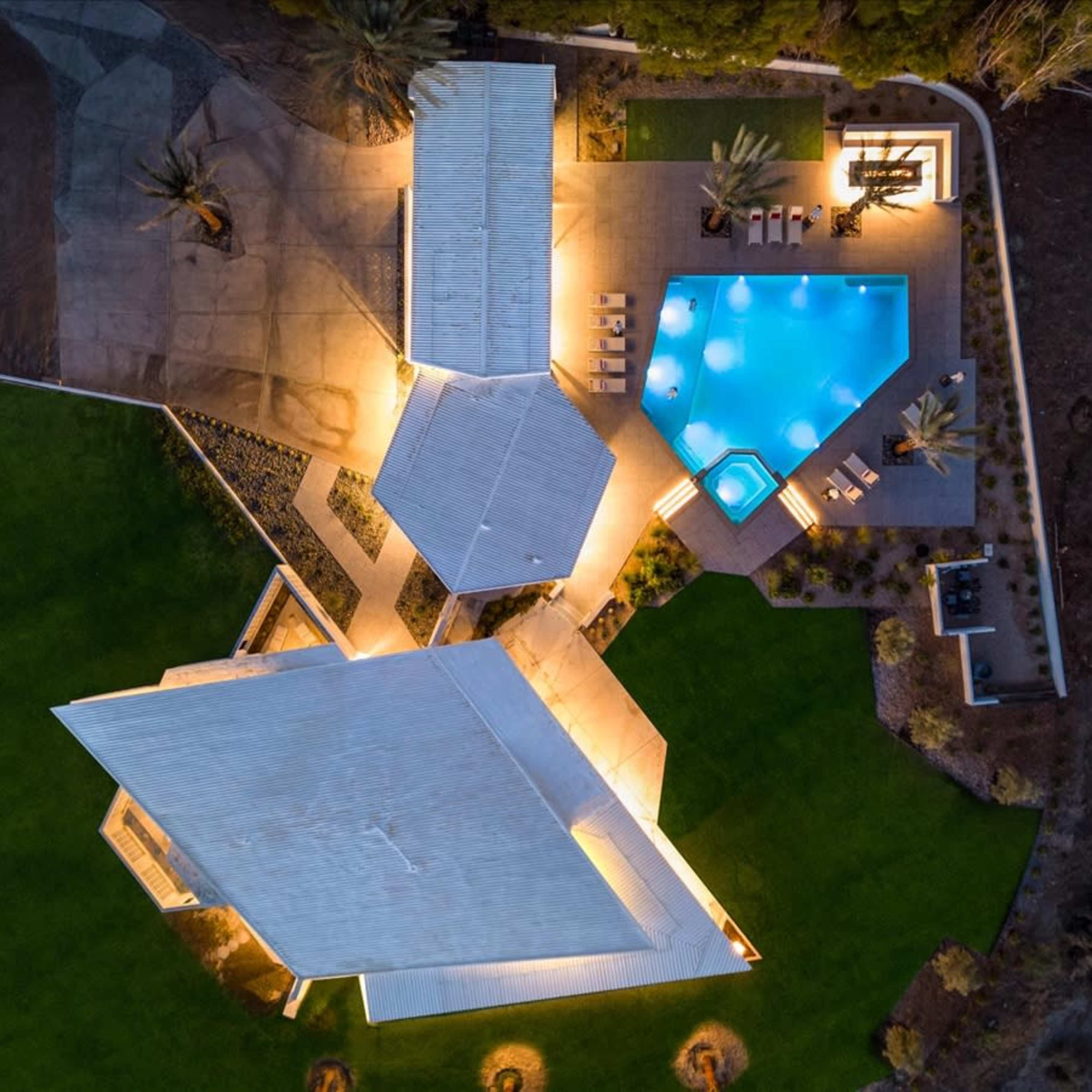 A modern architectural complex with three buildings surrounding a swimming pool and landscaped outdoor area, illuminated at night.