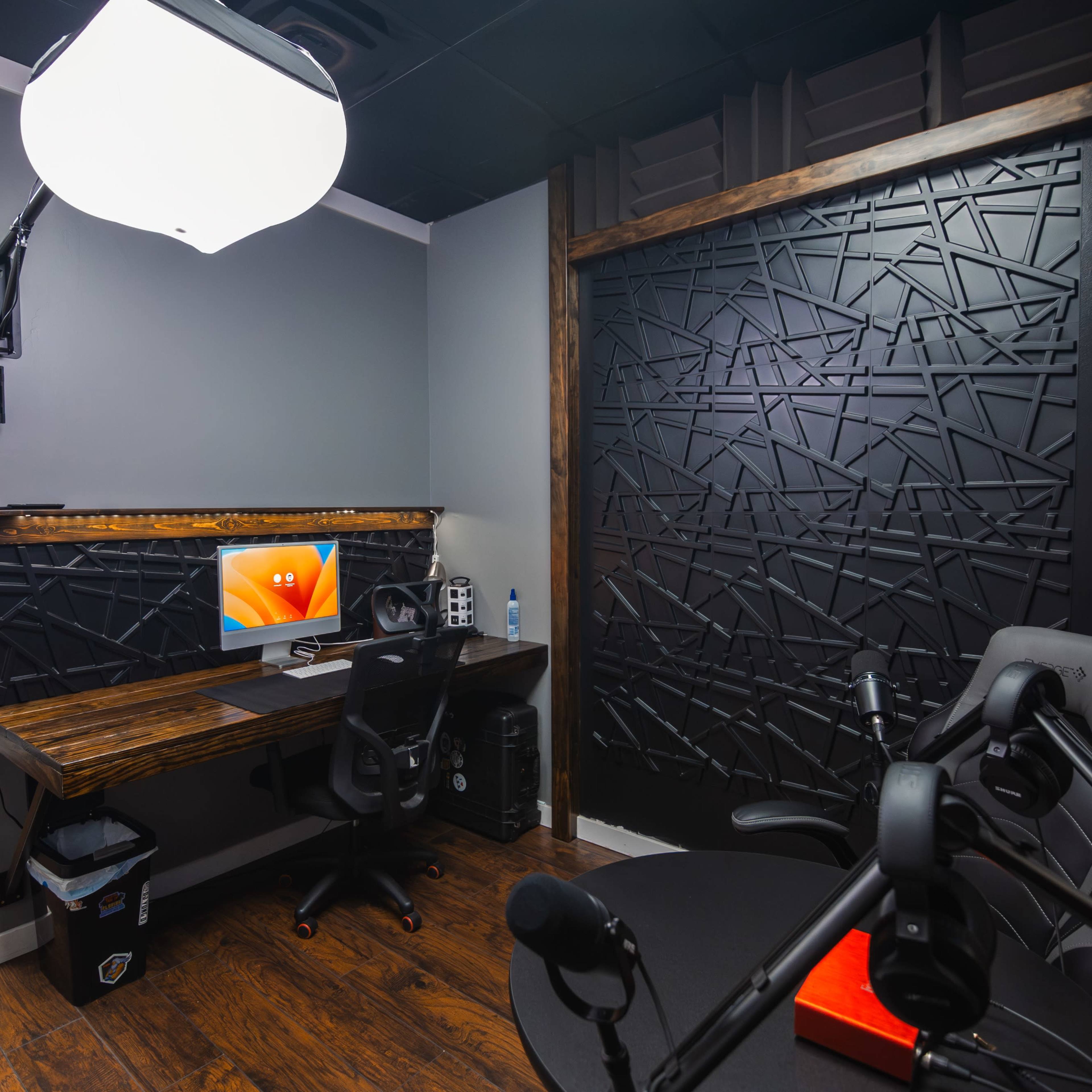 A small, modern office space featuring a wooden desk with a computer, a black ergonomic chair, and a dark, patterned wall.