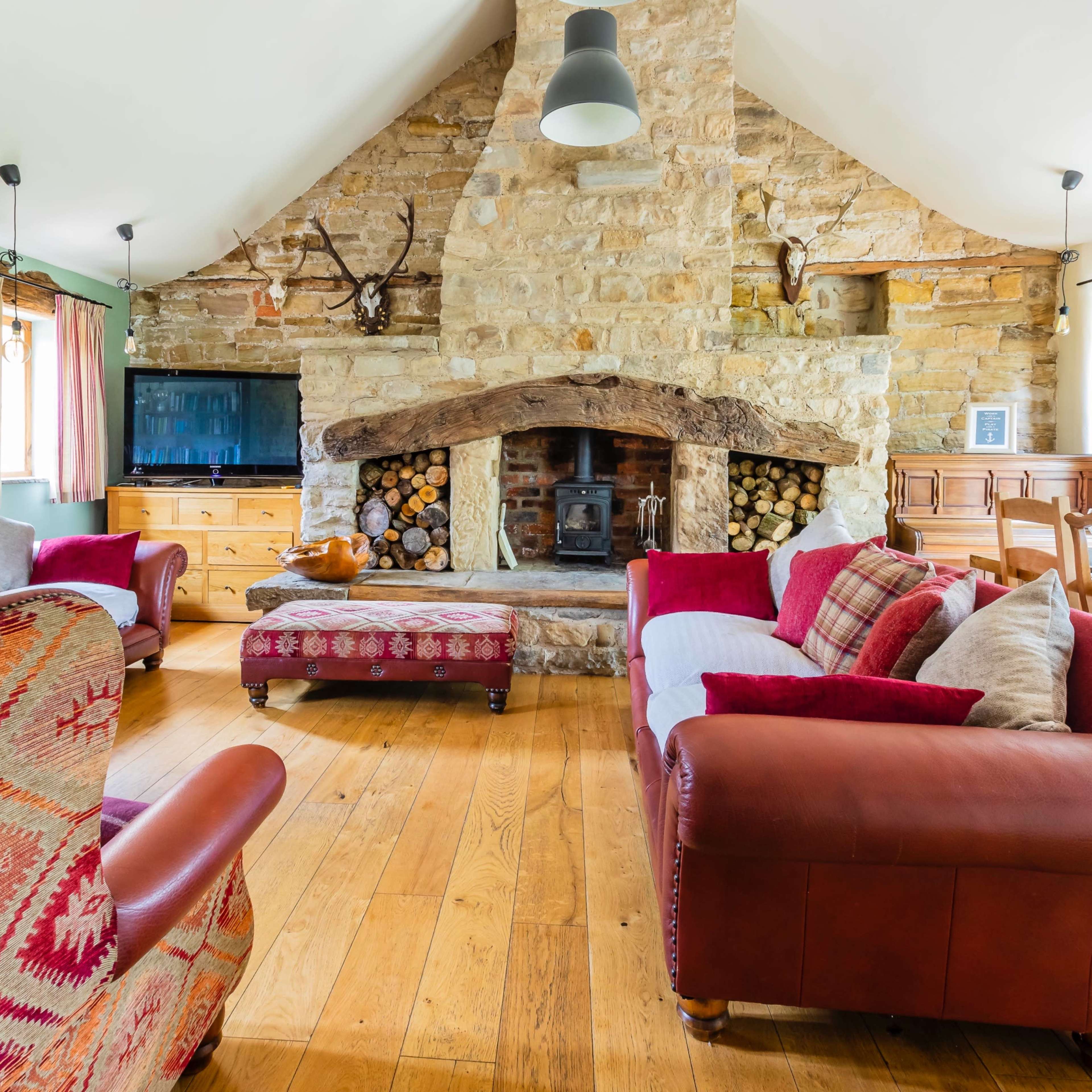 A cozy living room with a stone fireplace, wooden furniture, and large windows illuminating the space.