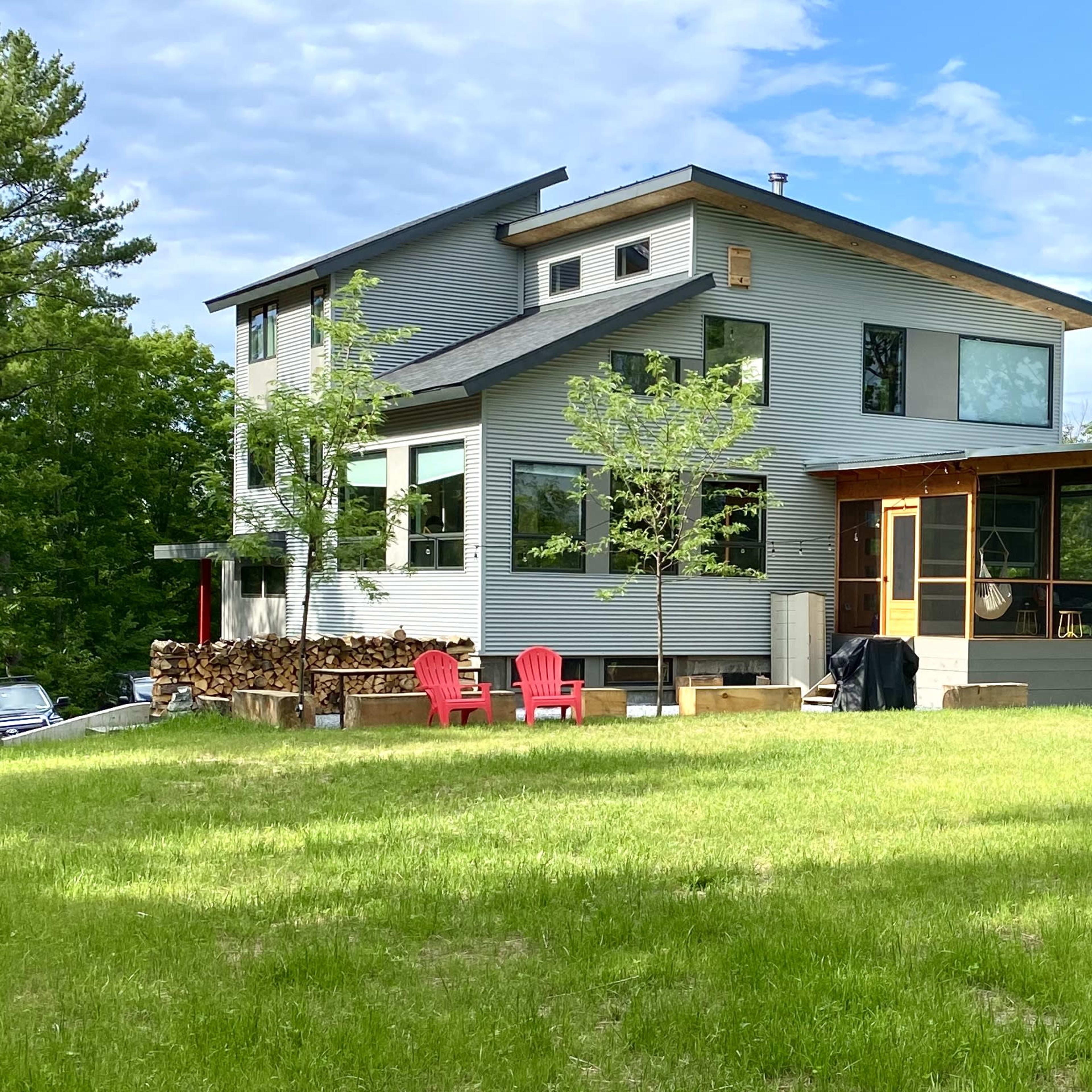 A modern house with large windows and a screened porch is set on a grassy lot surrounded by trees.