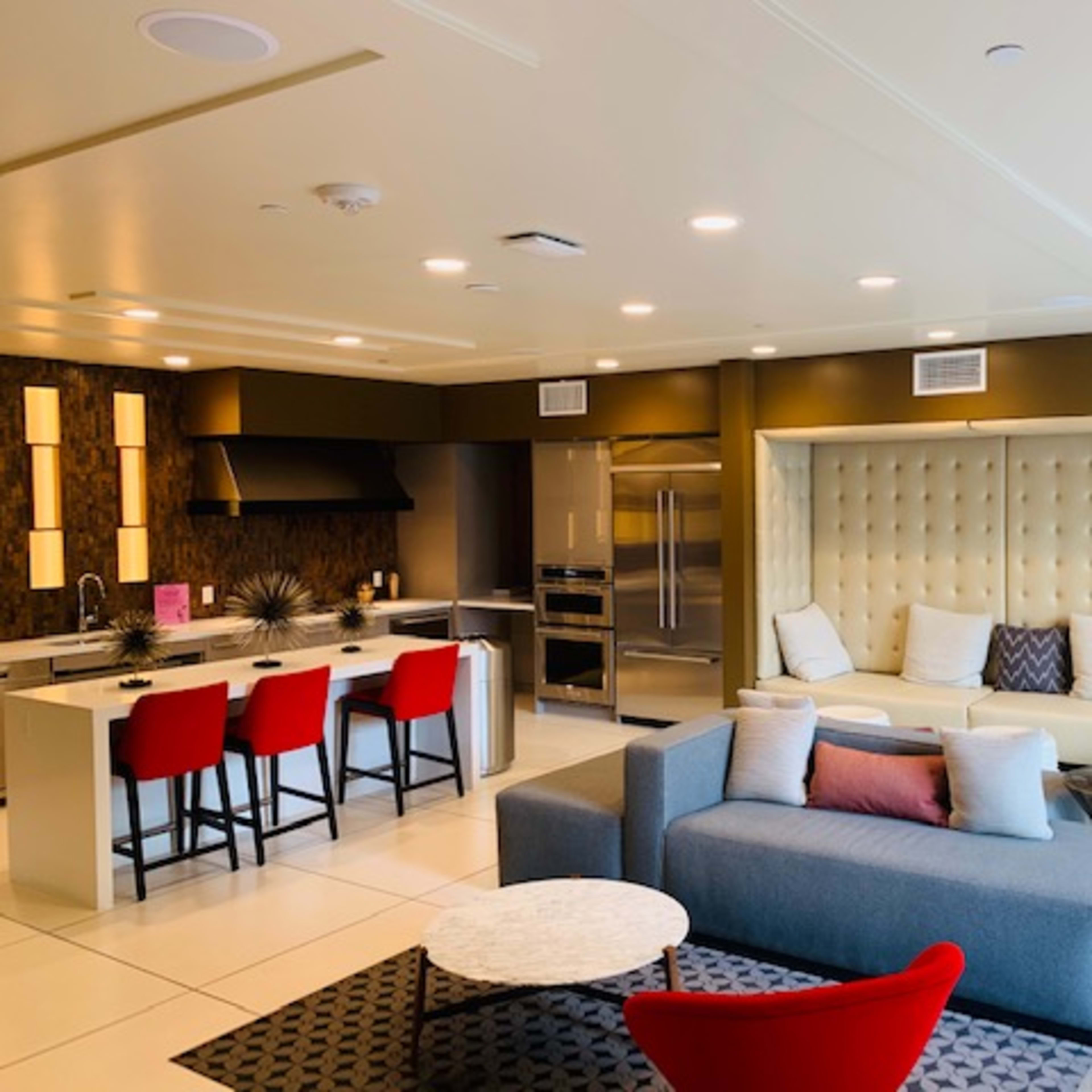 A modern living space featuring a kitchen with red bar stools, a sectional sofa, and a coffee table on a patterned rug.