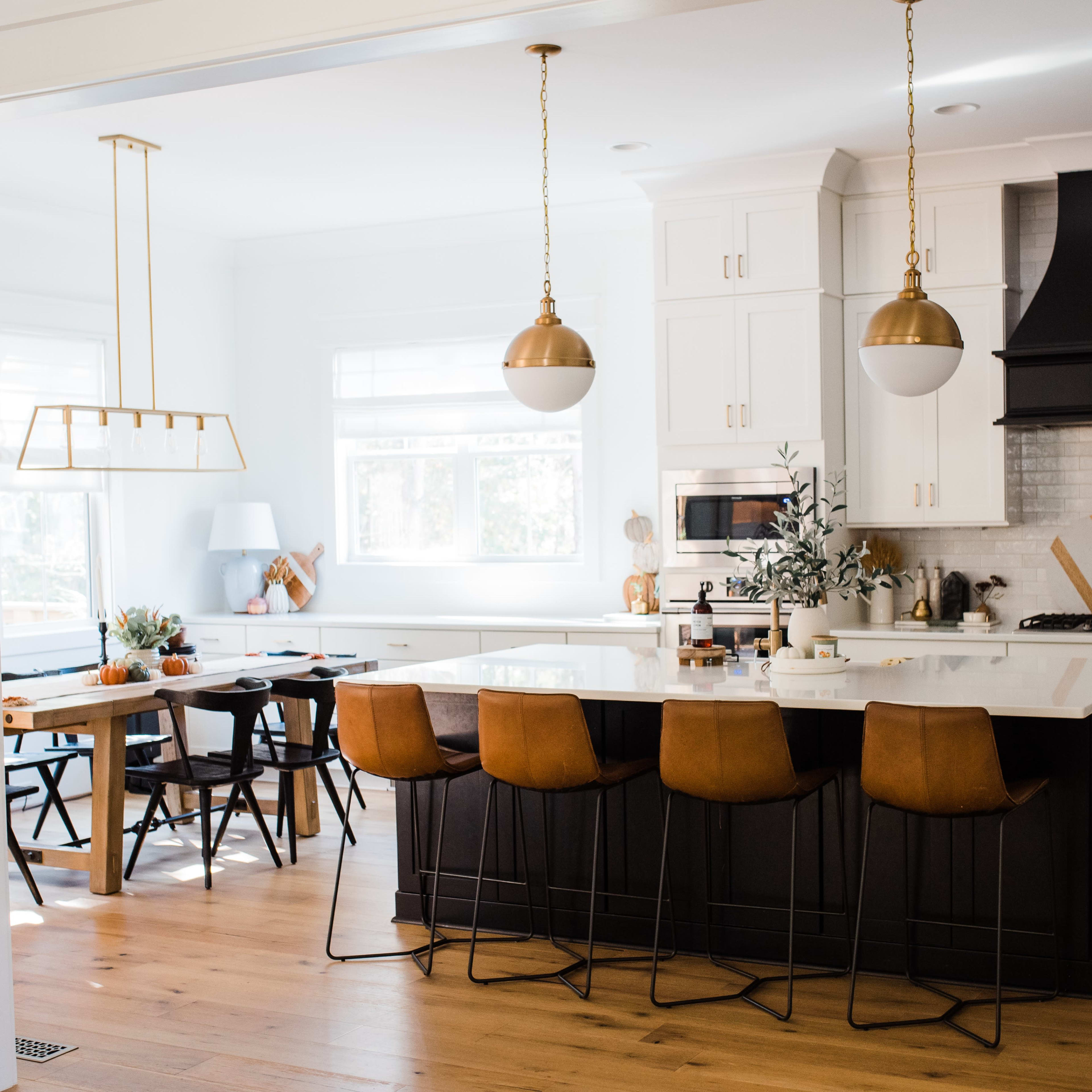 A modern kitchen with a large island featuring brown bar stools, a wooden dining table, and pendant lighting.
