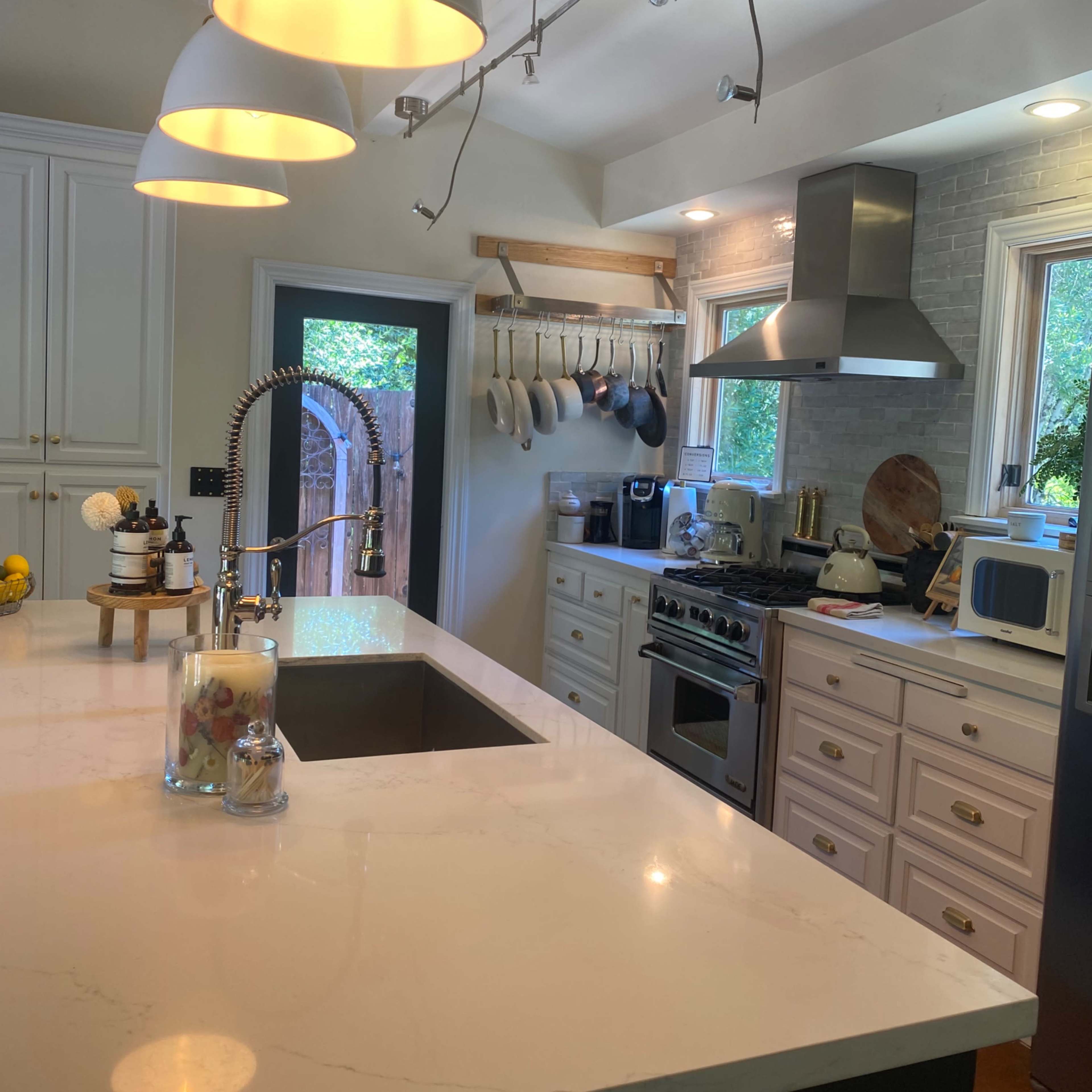 A modern kitchen with a large island featuring a sink, stainless steel appliances, and white cabinetry, illuminated by pendant lights.
