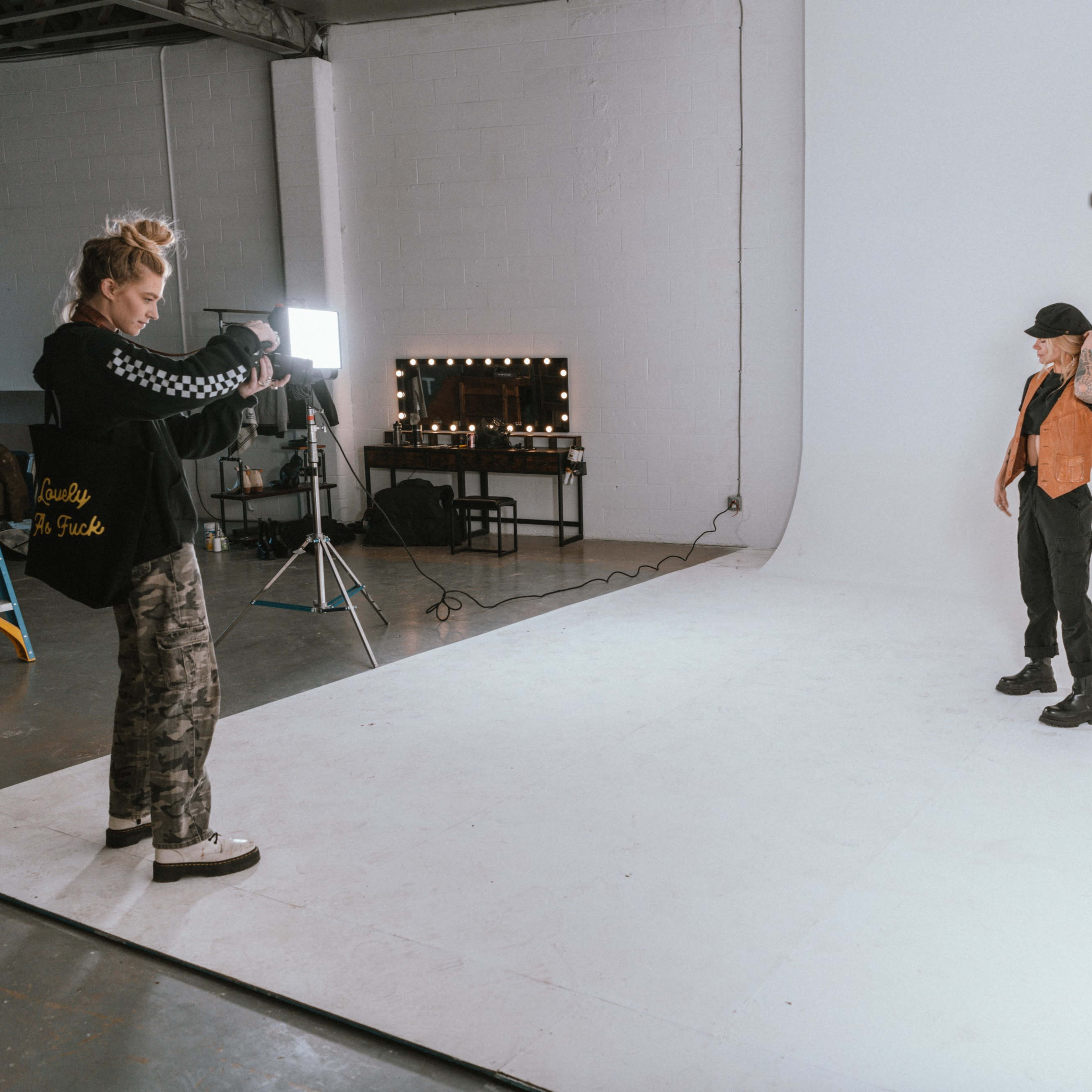 A photographer captures a model posing in front of a plain white backdrop in a studio.