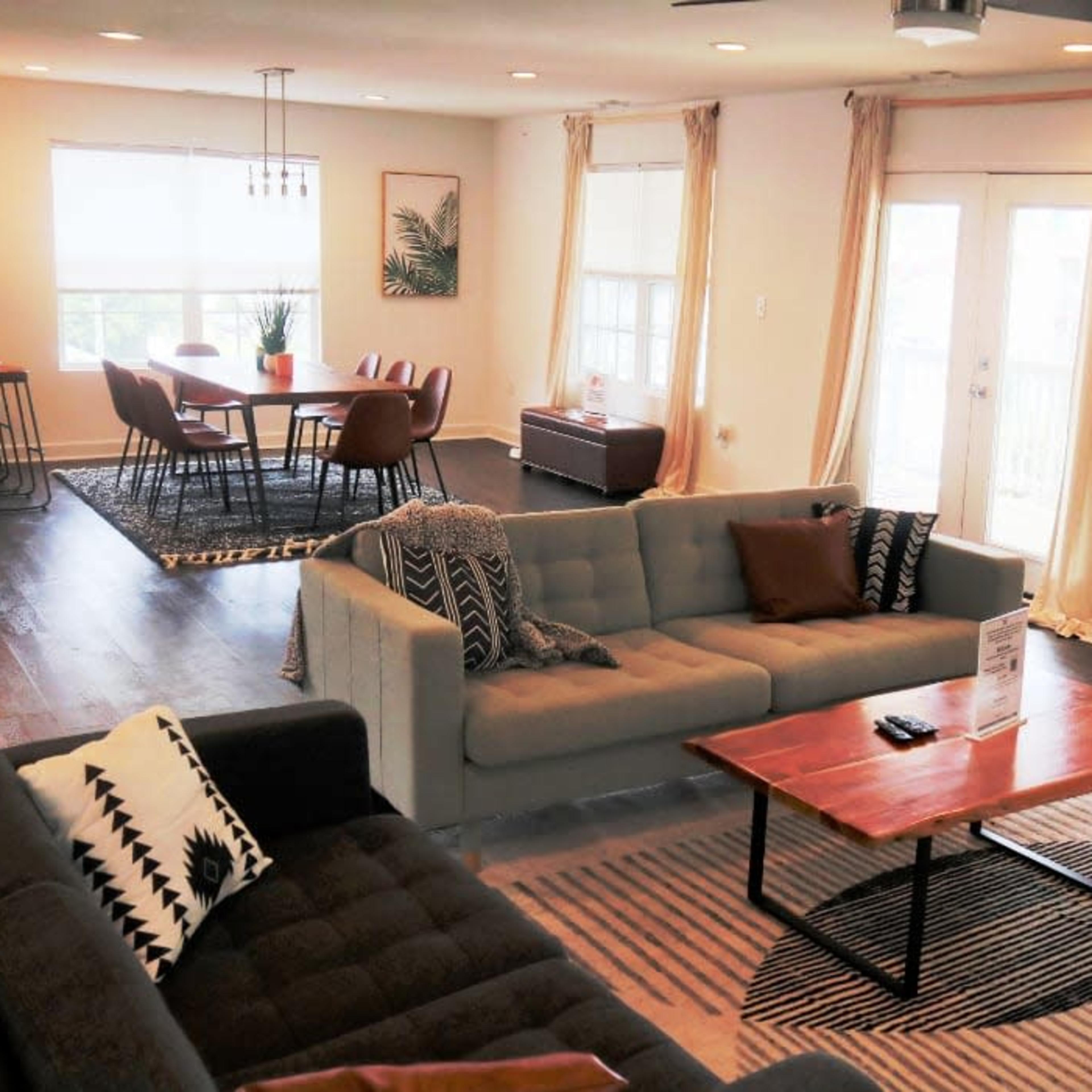 A spacious living area features two sofas facing a coffee table, with a dining table and chairs visible in the background.
