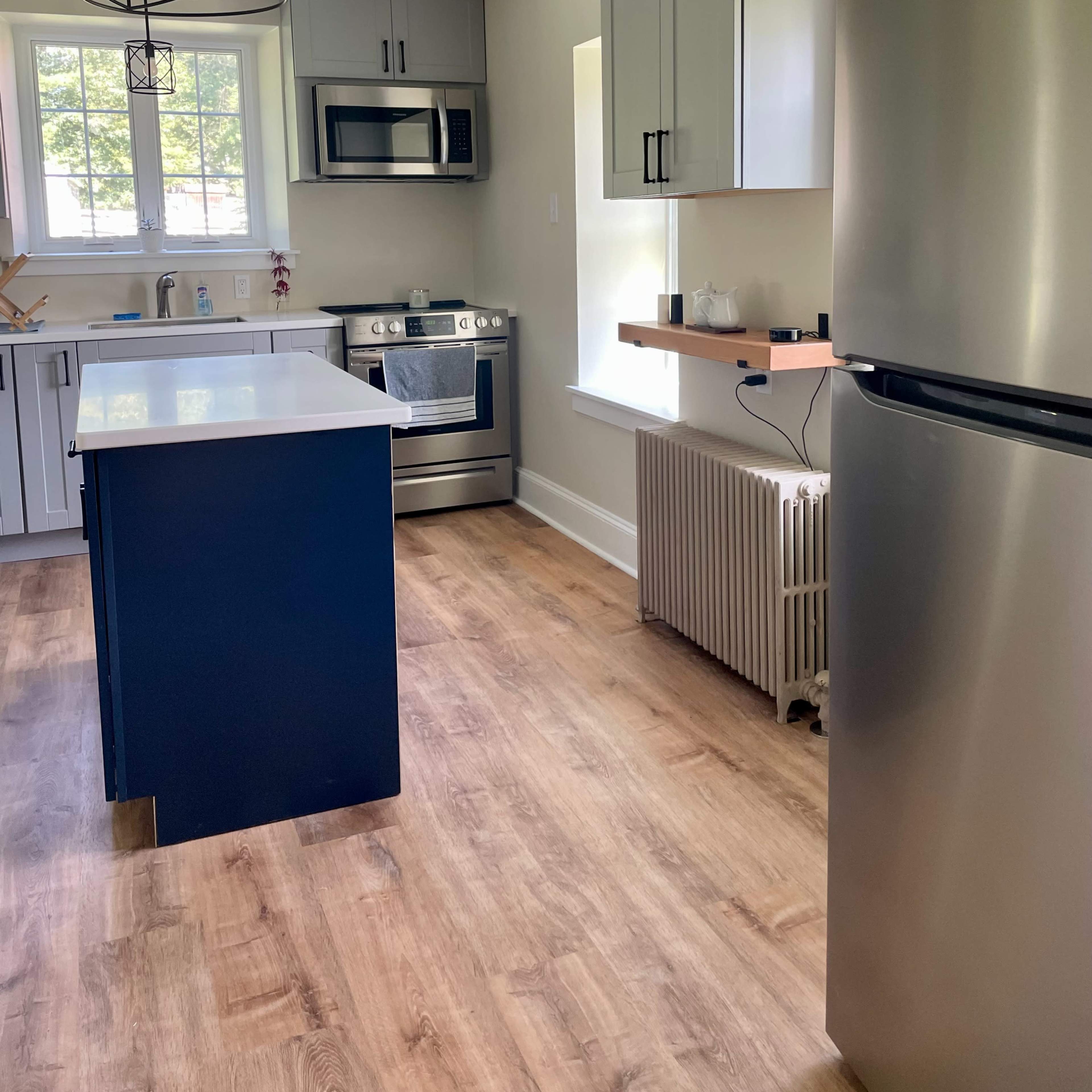 A modern kitchen featuring stainless steel appliances, a central island with a blue base, and light wood flooring.