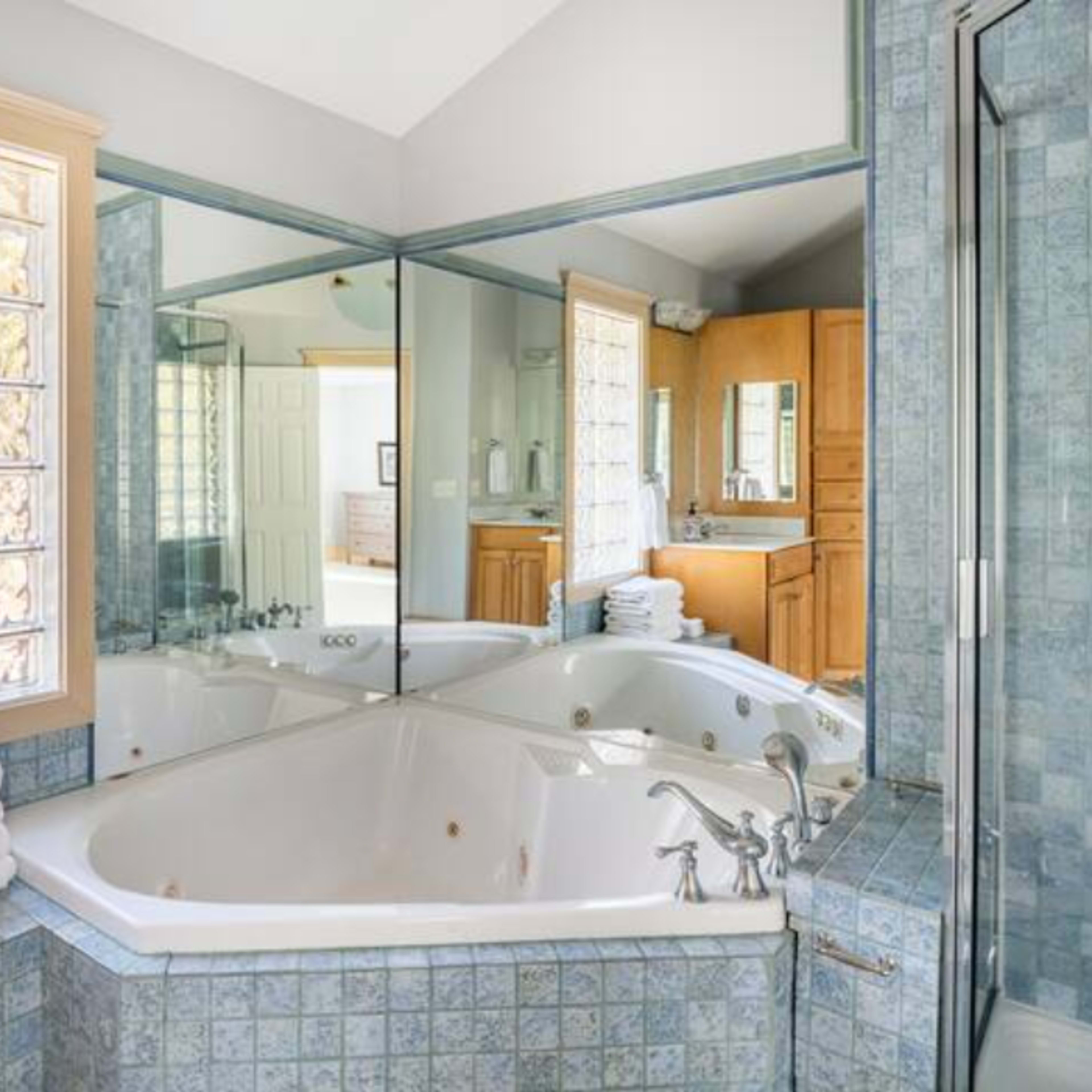 A spacious bathroom featuring a large corner bathtub surrounded by blue tiled walls and a wall of glass blocks that allows natural light in.