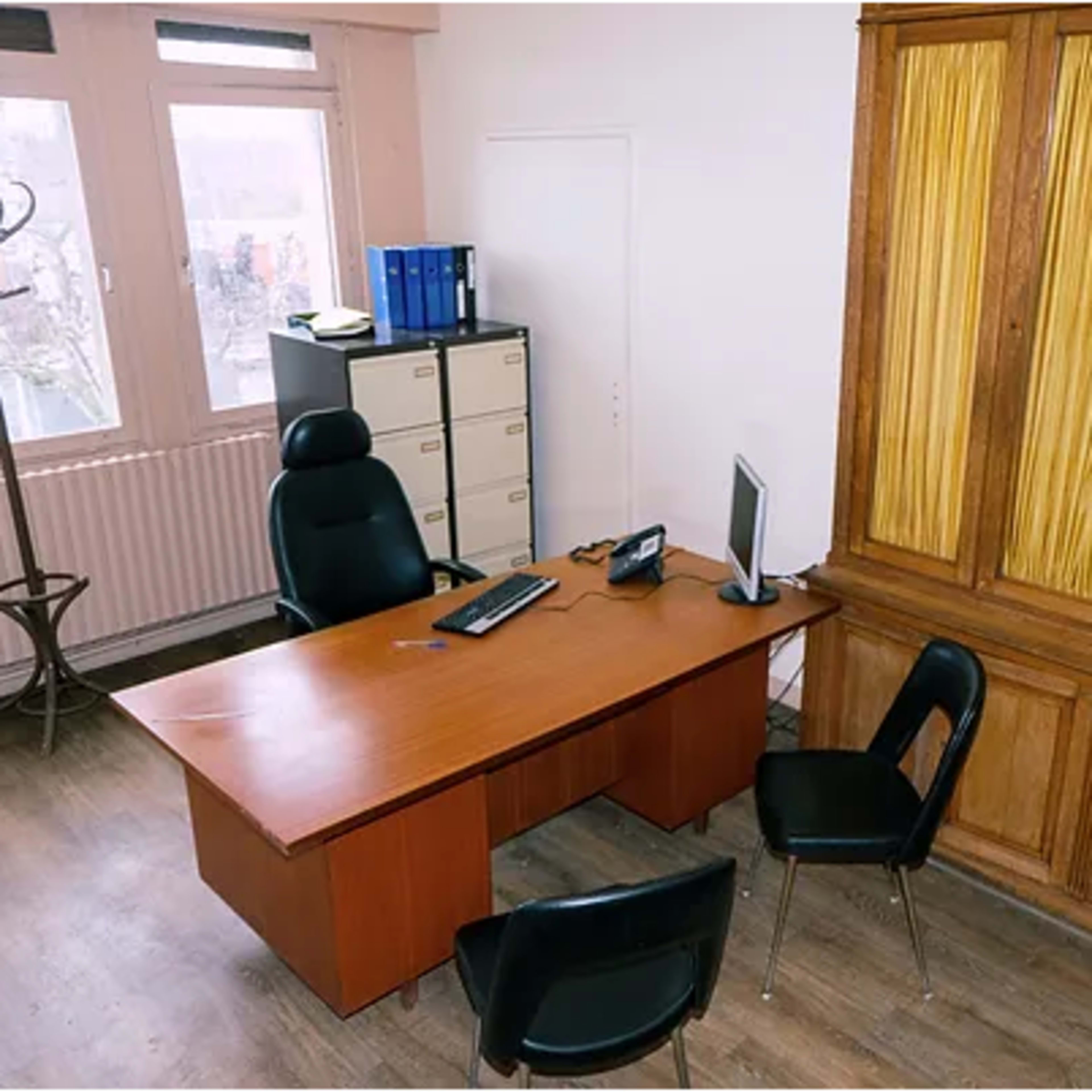 An office with a wooden desk, two black chairs, a computer monitor, and a wooden cabinet against the wall.