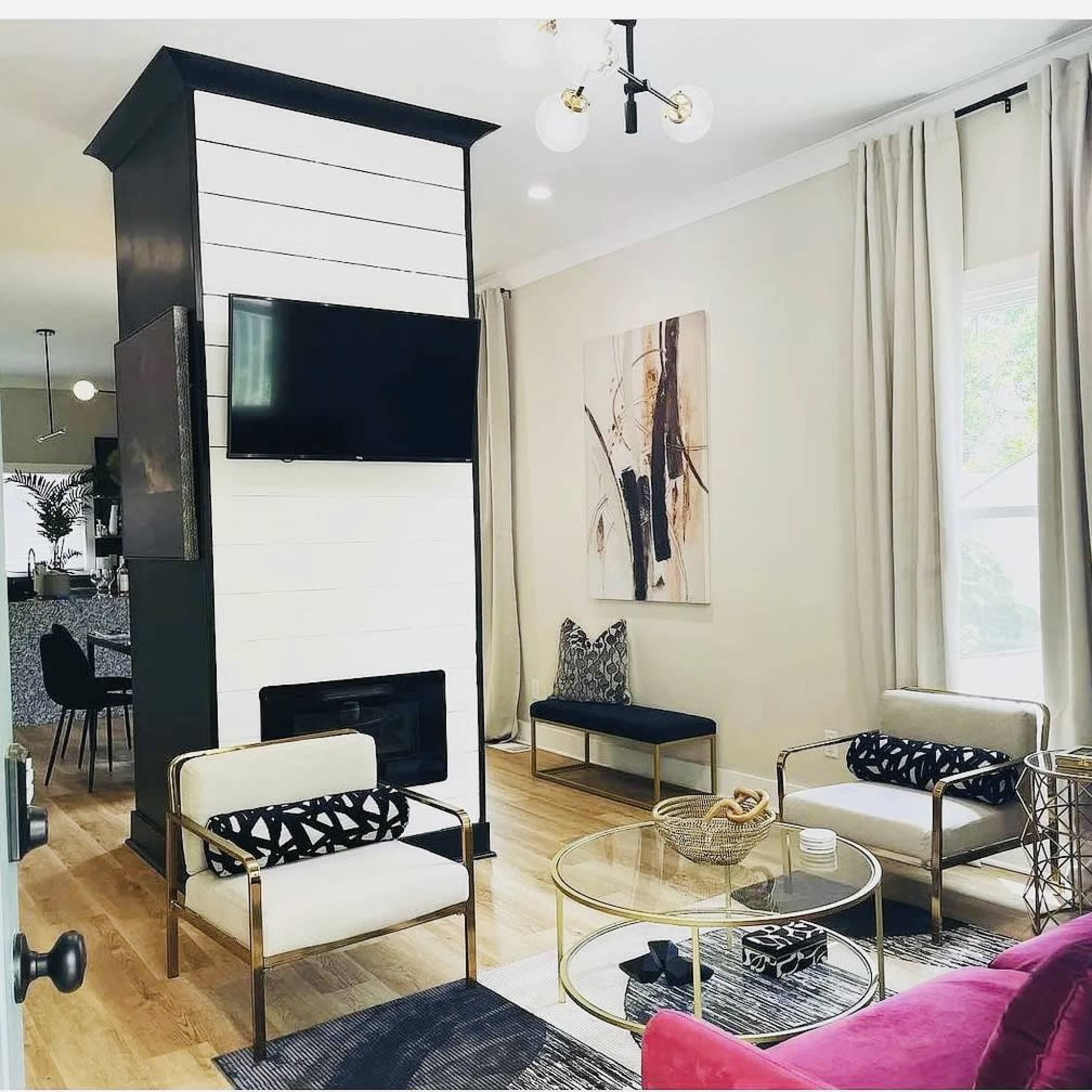 A modern living room features a black and white fireplace, a wall-mounted television, and two seating areas with stylish furniture.