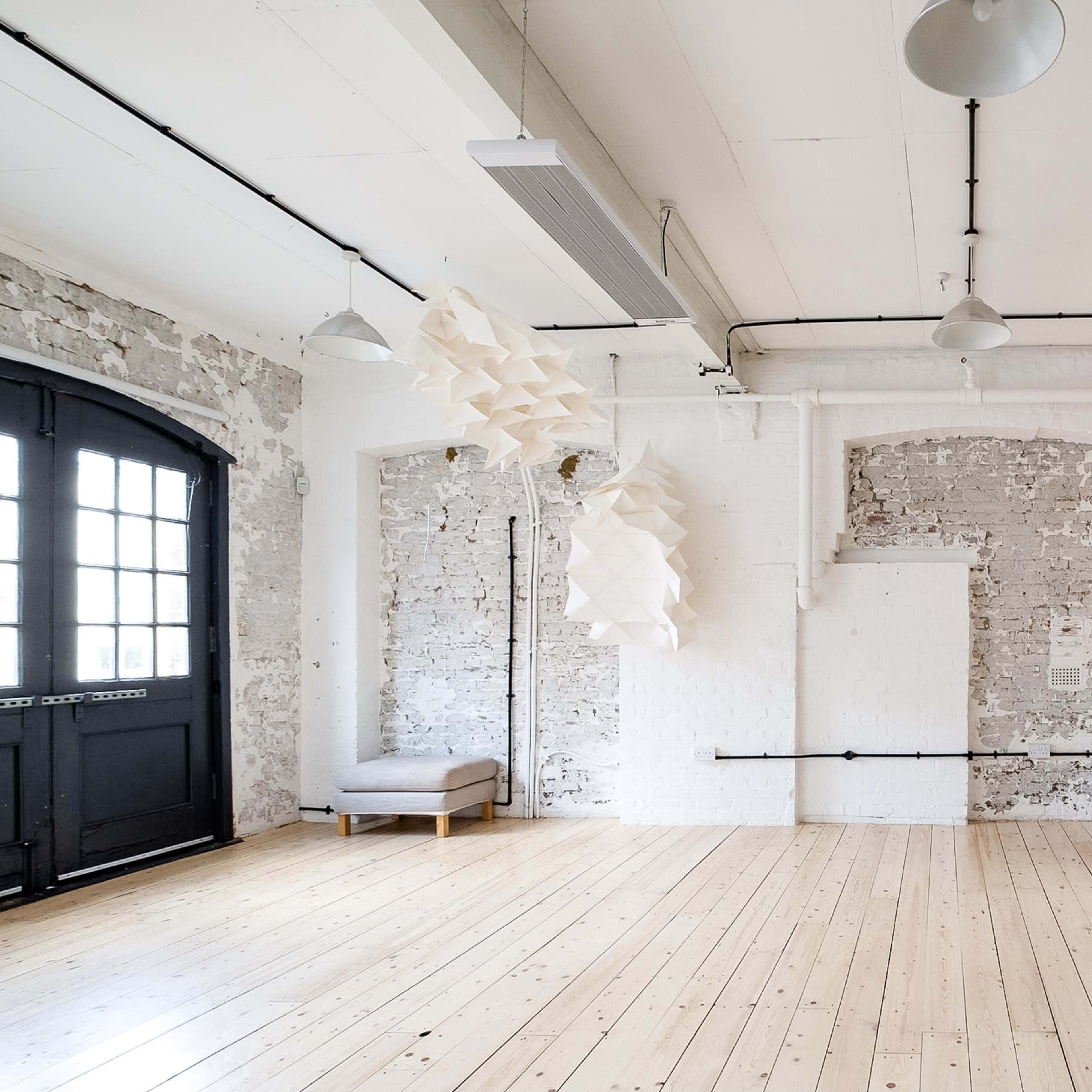 A bright, minimalist interior of a room with exposed brick walls, wooden flooring, and a modern light fixture hanging from the ceiling.