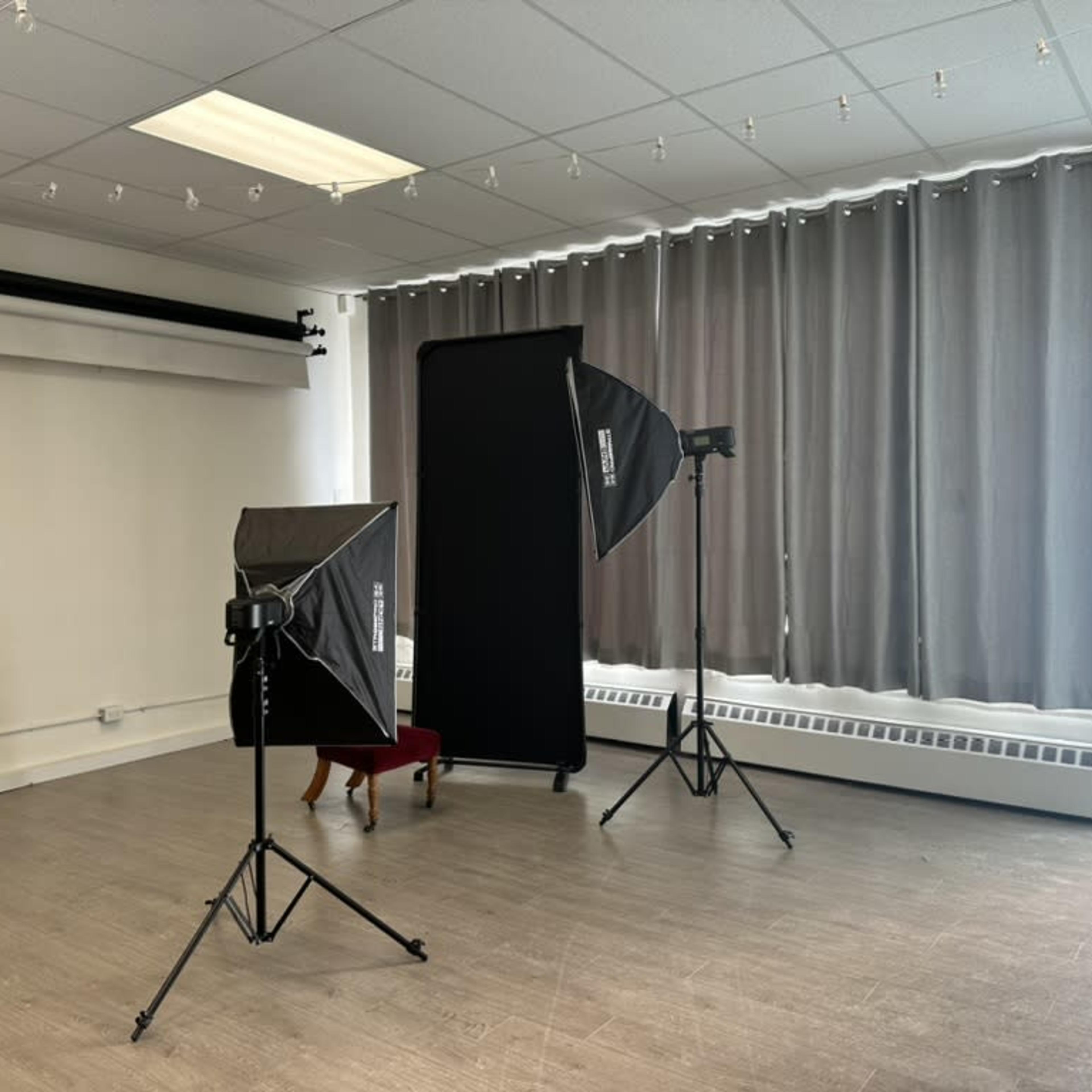 A photography studio with two softboxes, a backdrop holder, and large curtains covering a window.