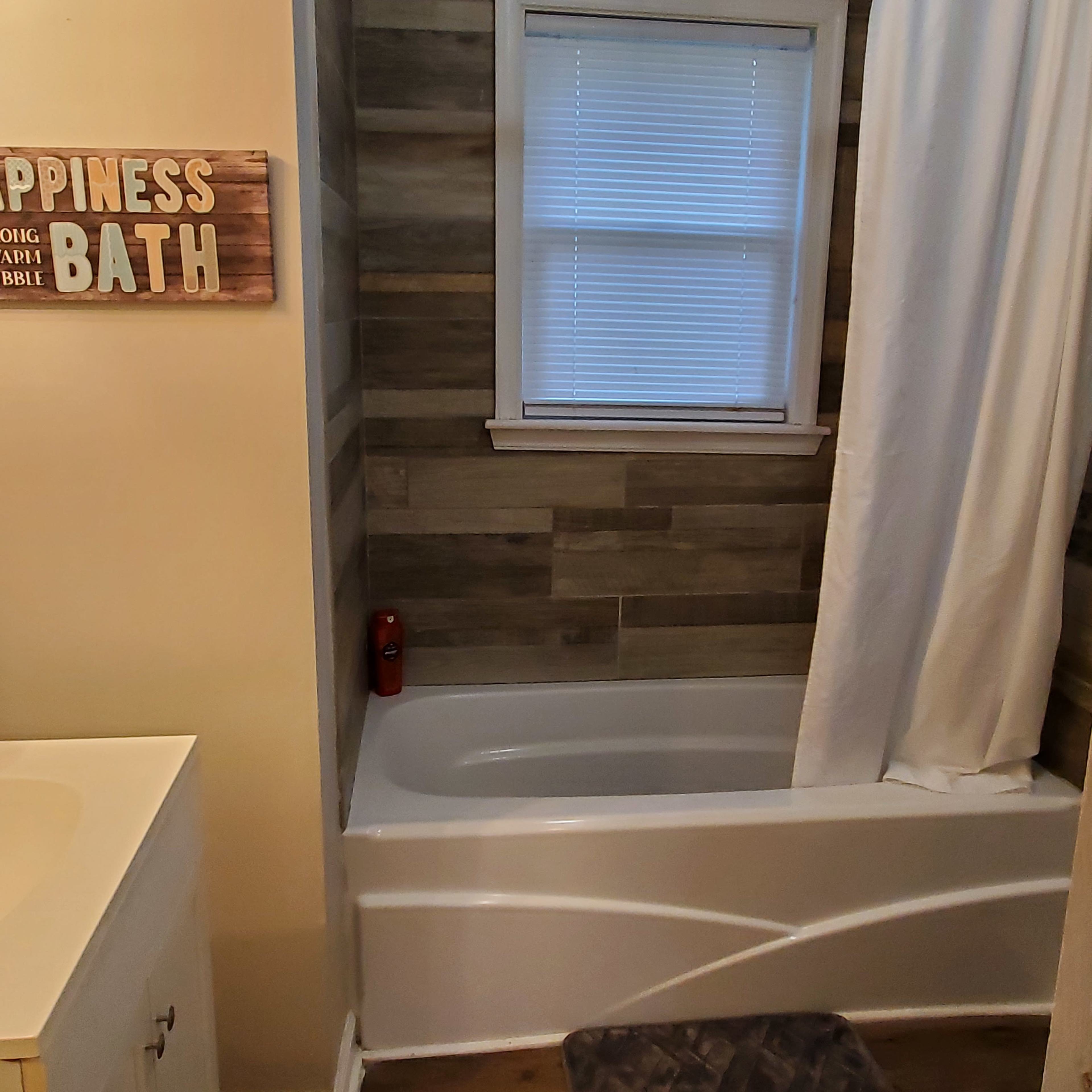 A bathroom with a bathtub, a shower curtain, and wooden wall panels, alongside a sign that reads "Happiness Bath."