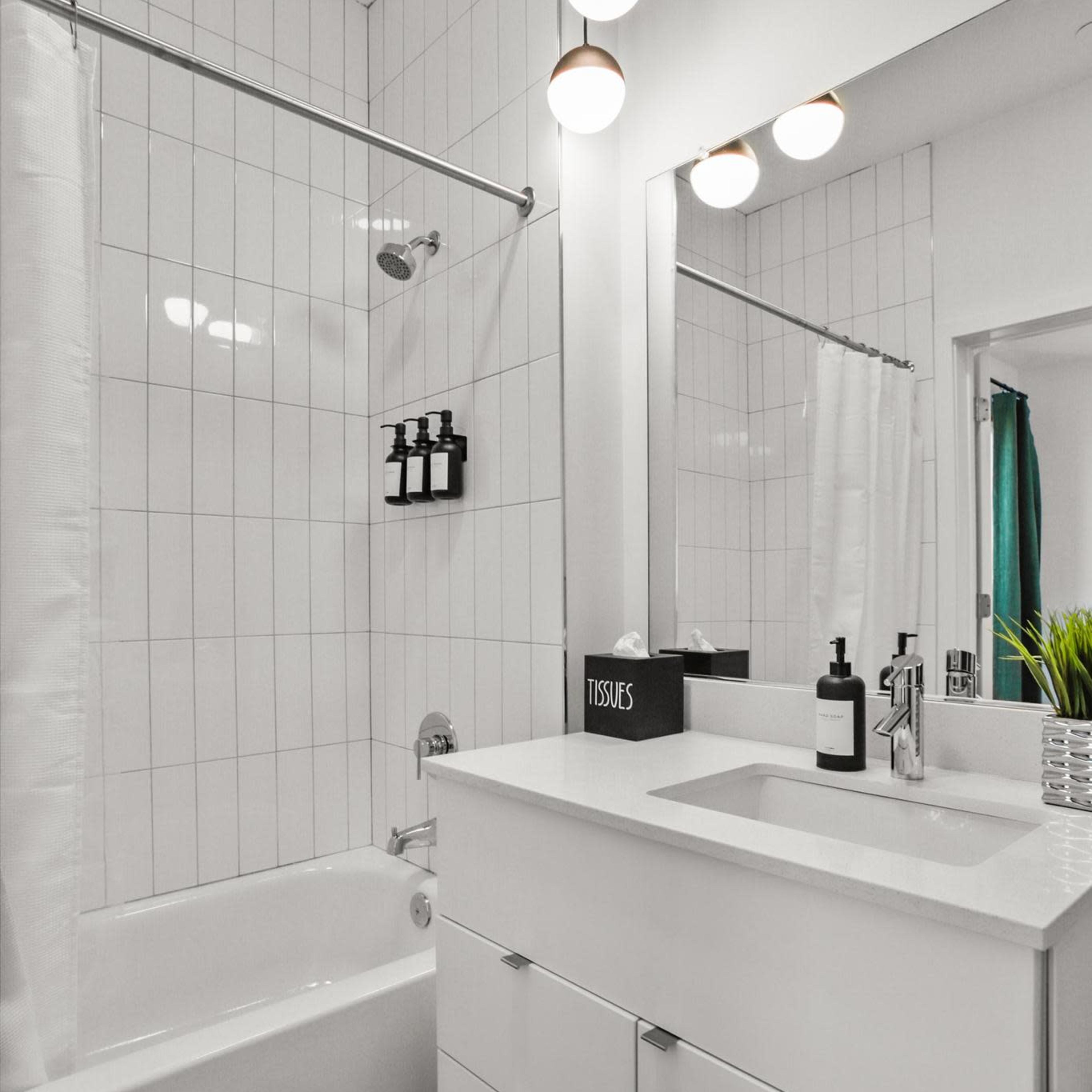 A modern bathroom featuring a white bathtub, a sleek sink with a mirror above, and a tiled wall with hanging toiletries.