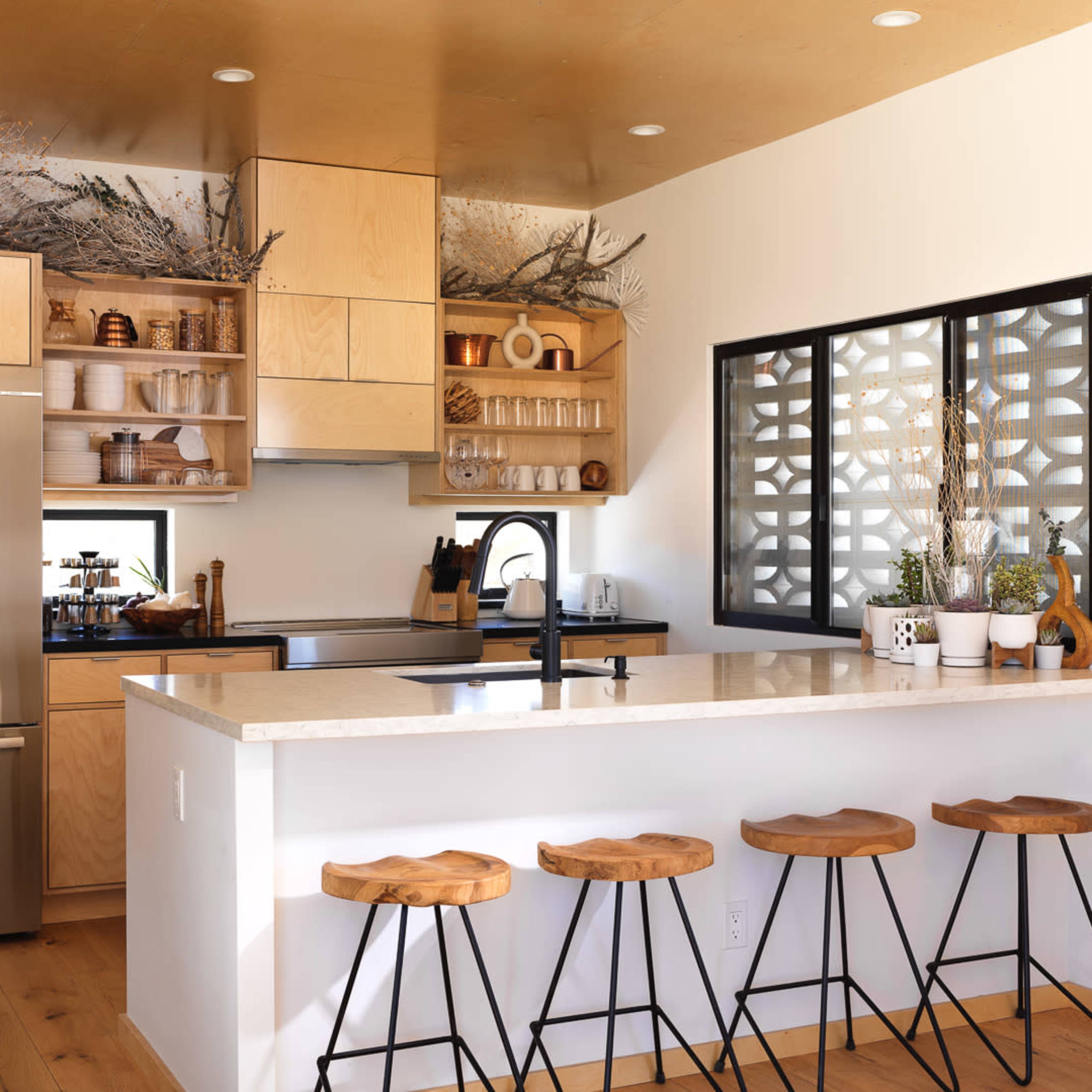 A modern kitchen features wooden cabinetry, a stainless steel refrigerator, and a countertop with bar stools.