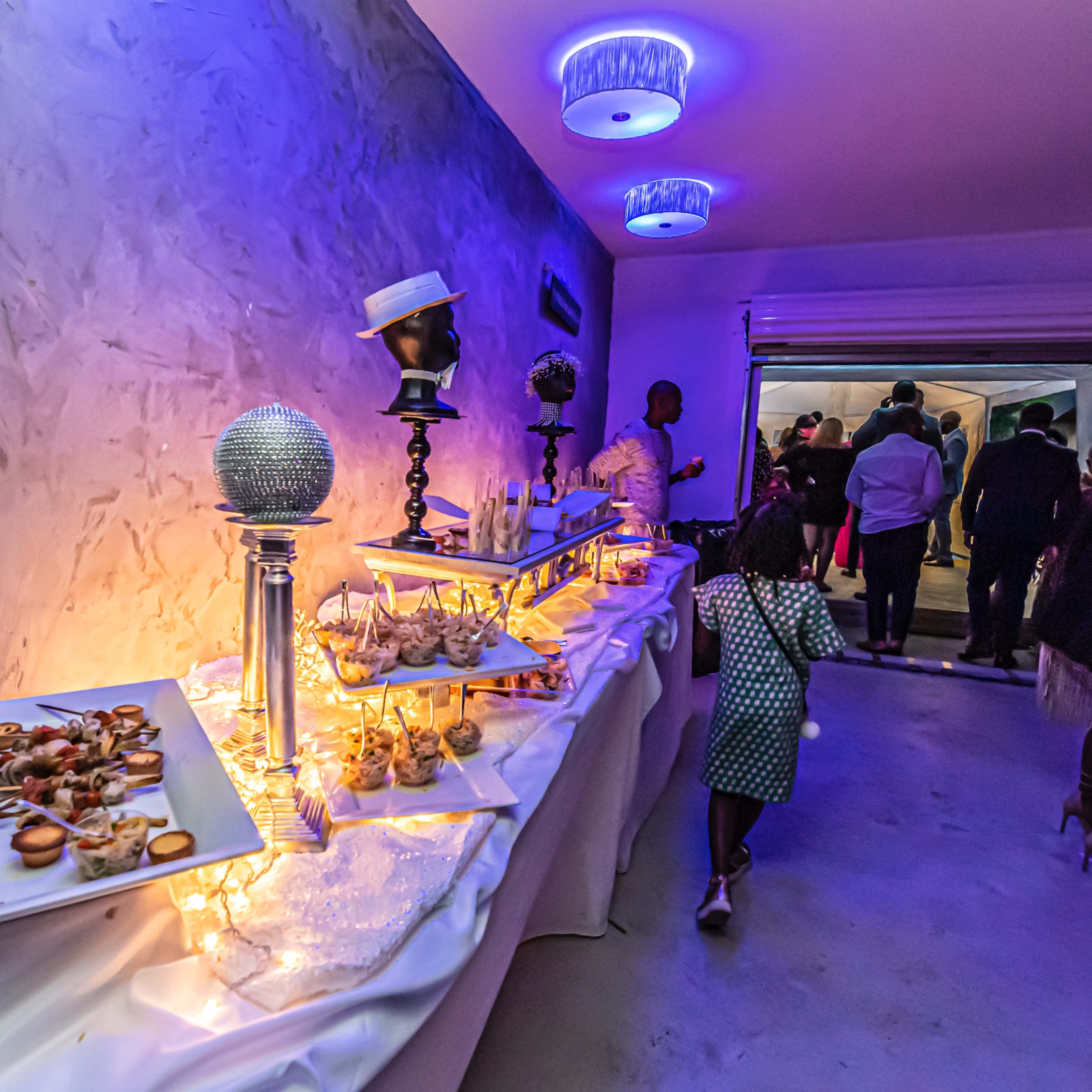 A buffet table adorned with various appetizers and decorative elements is set up in a dimly lit room, with guests mingling in the background.