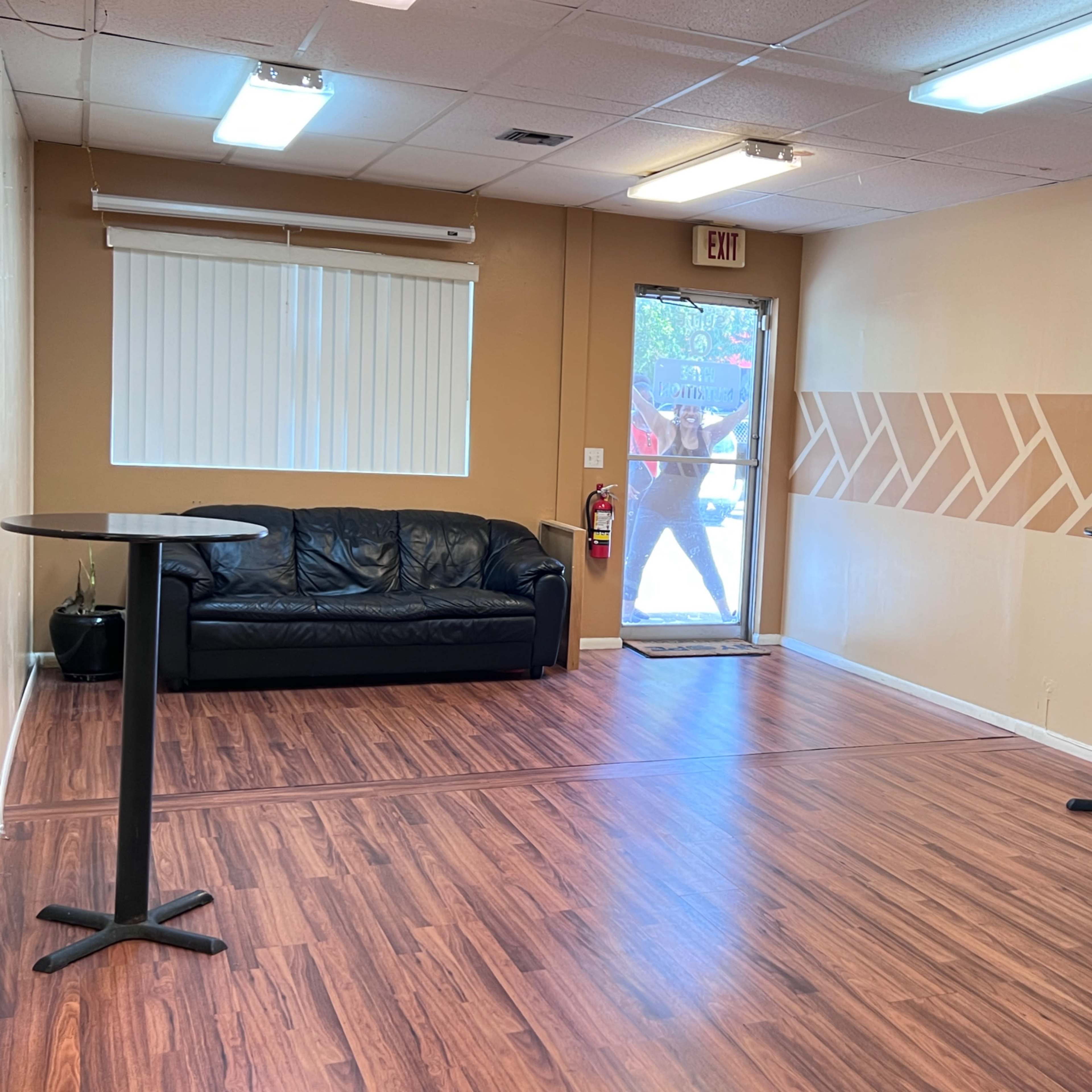 A sparsely furnished room with a black couch, two small tables, and a door leading outside.
