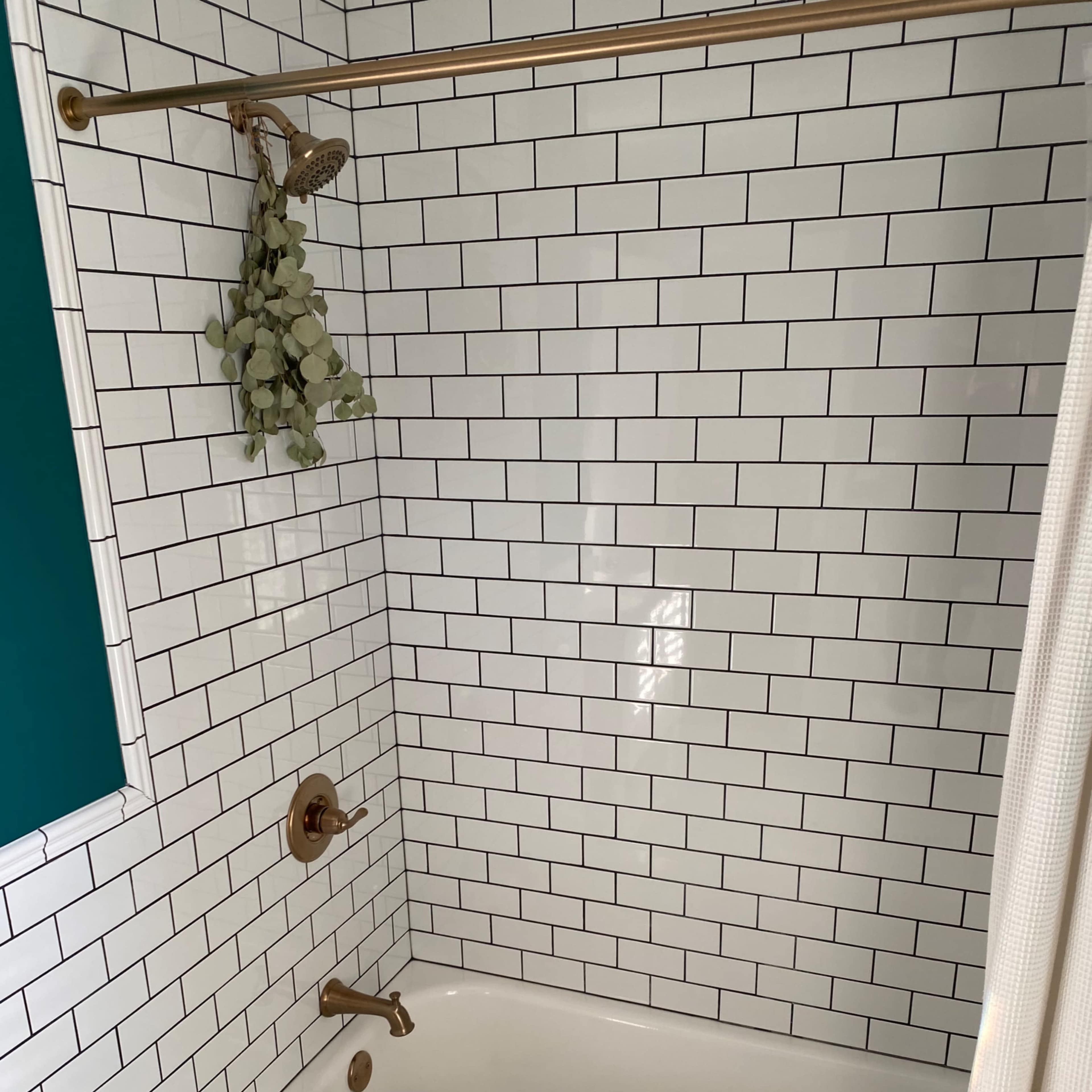 A bathroom shower area with white subway tiles, a bathtub, and a towel on the floor.