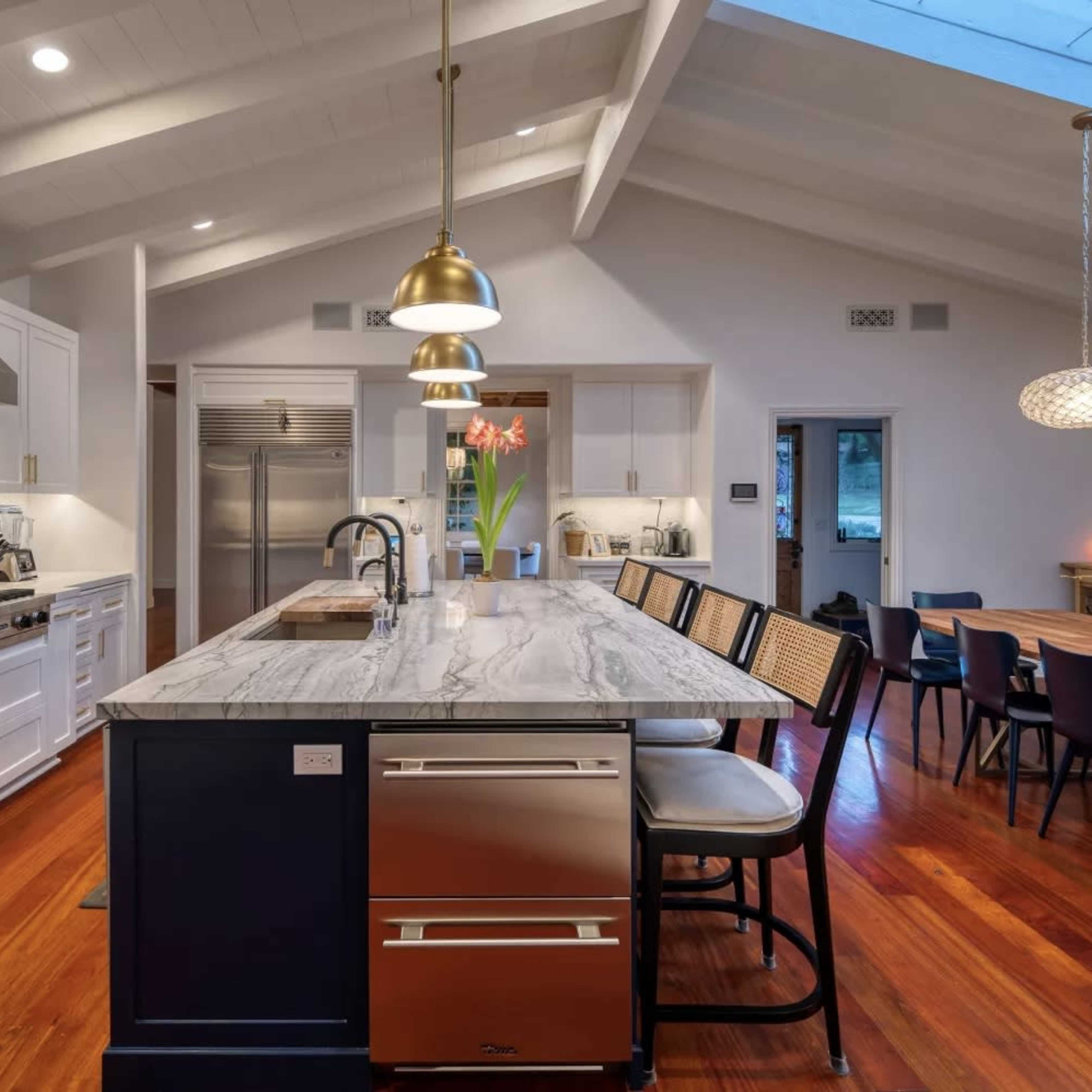 A modern kitchen featuring a large island with a marble countertop, stainless steel appliances, and wooden beams on the ceiling.