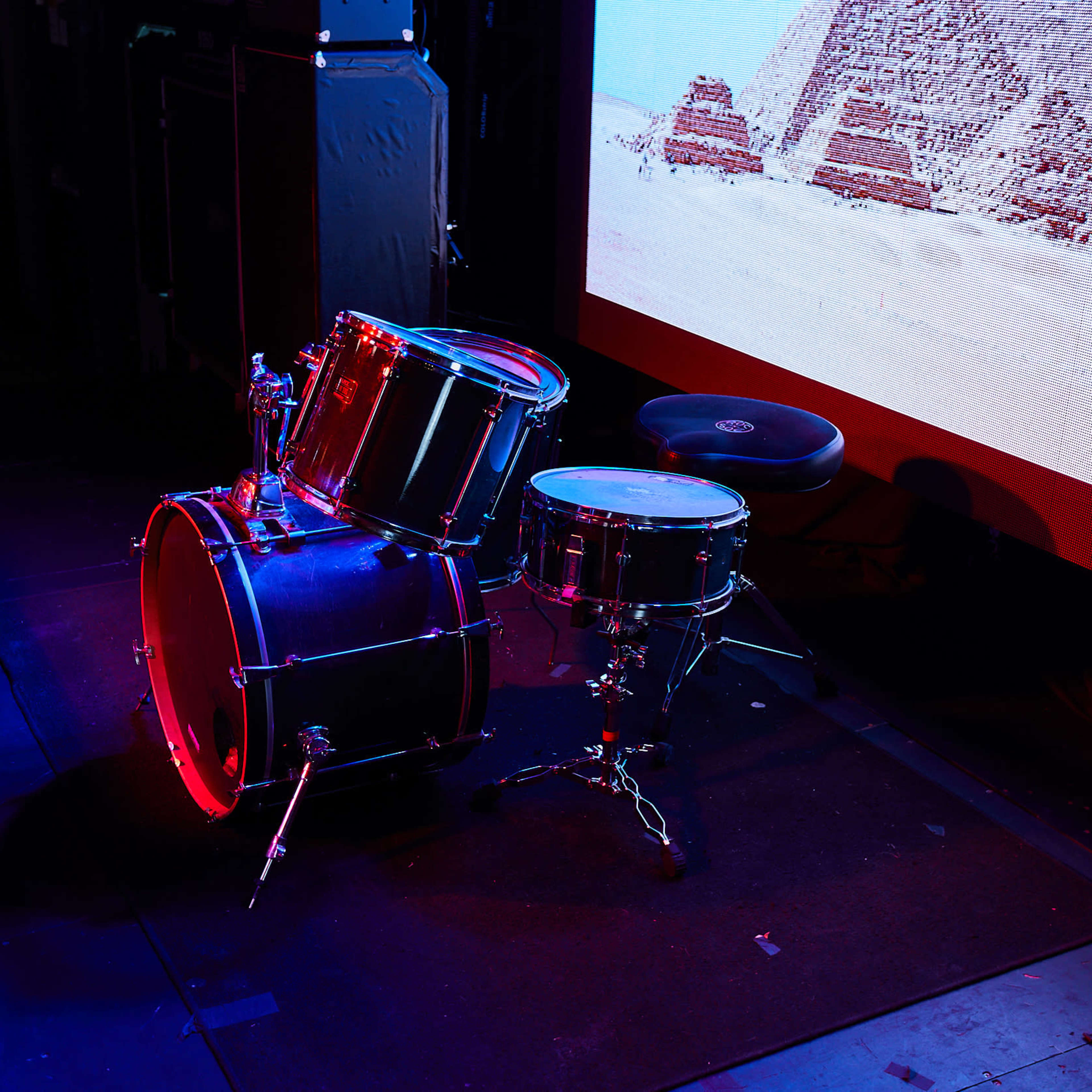 A black drum set is positioned in front of a large screen displaying an image of pyramids.