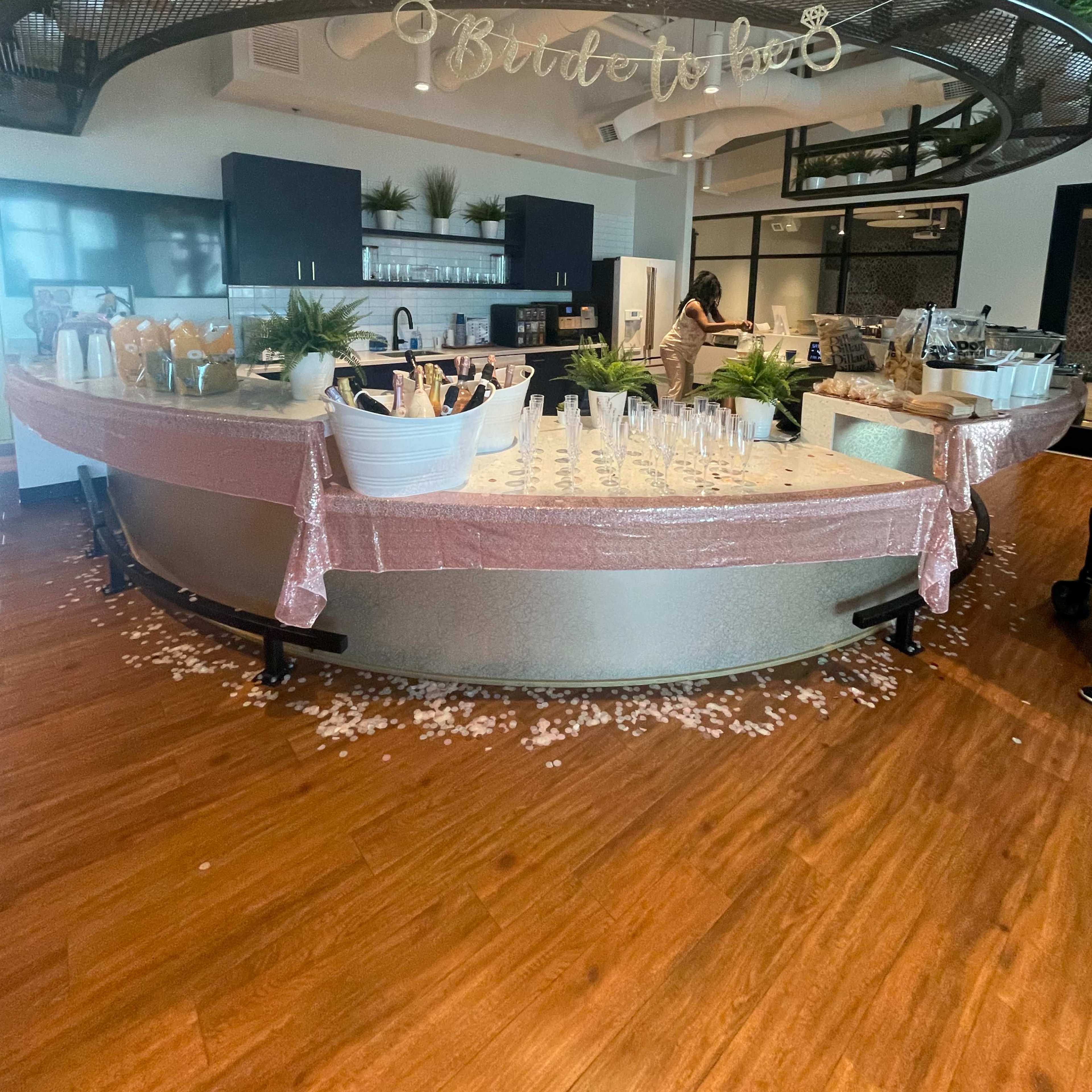 A modern event space featuring a circular bar setup adorned with decorative elements and a variety of glassware, set against stylish kitchen facilities.