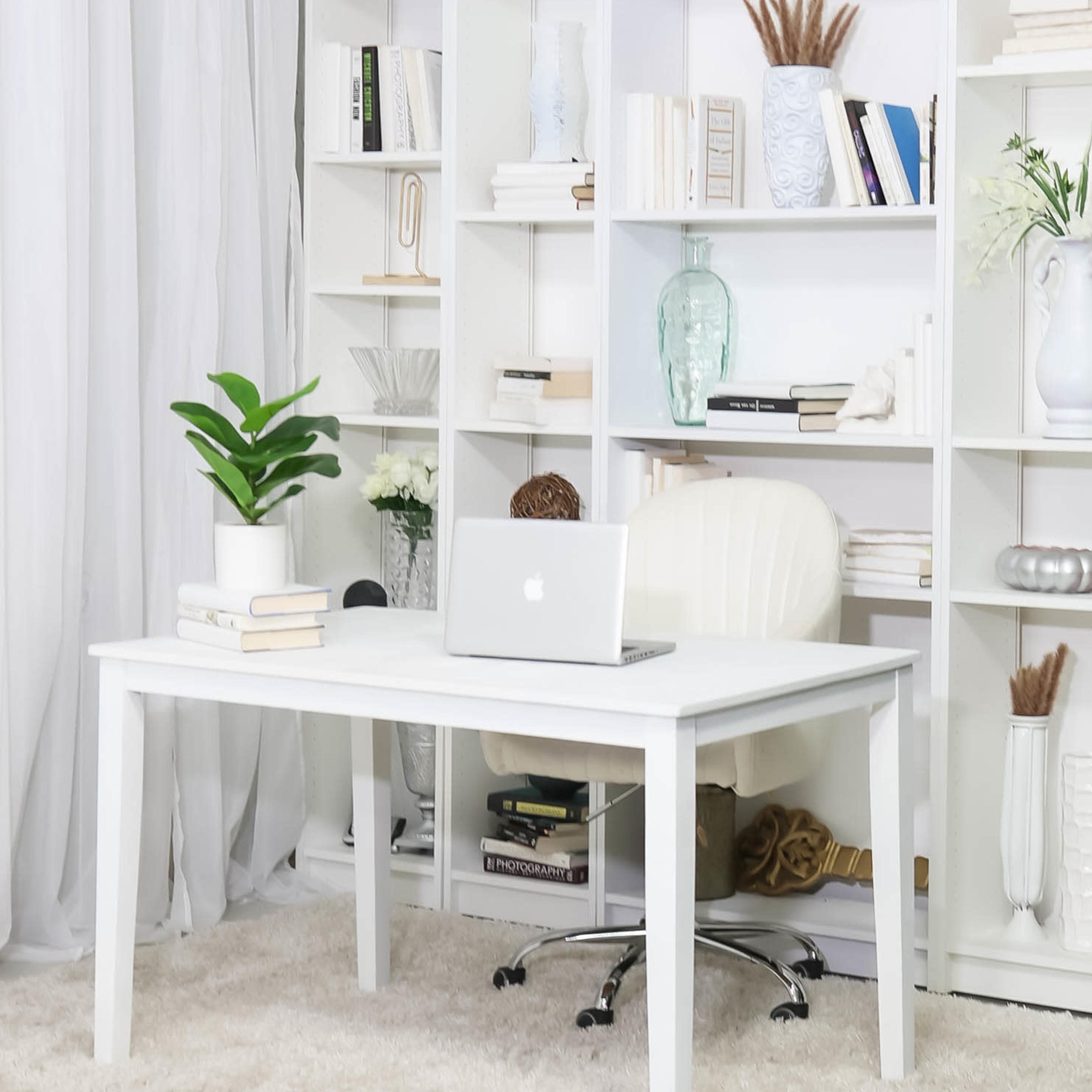 A minimalist home office features a white desk and chair in front of a bookshelf filled with books and decorative items, with a potted plant on the desk.