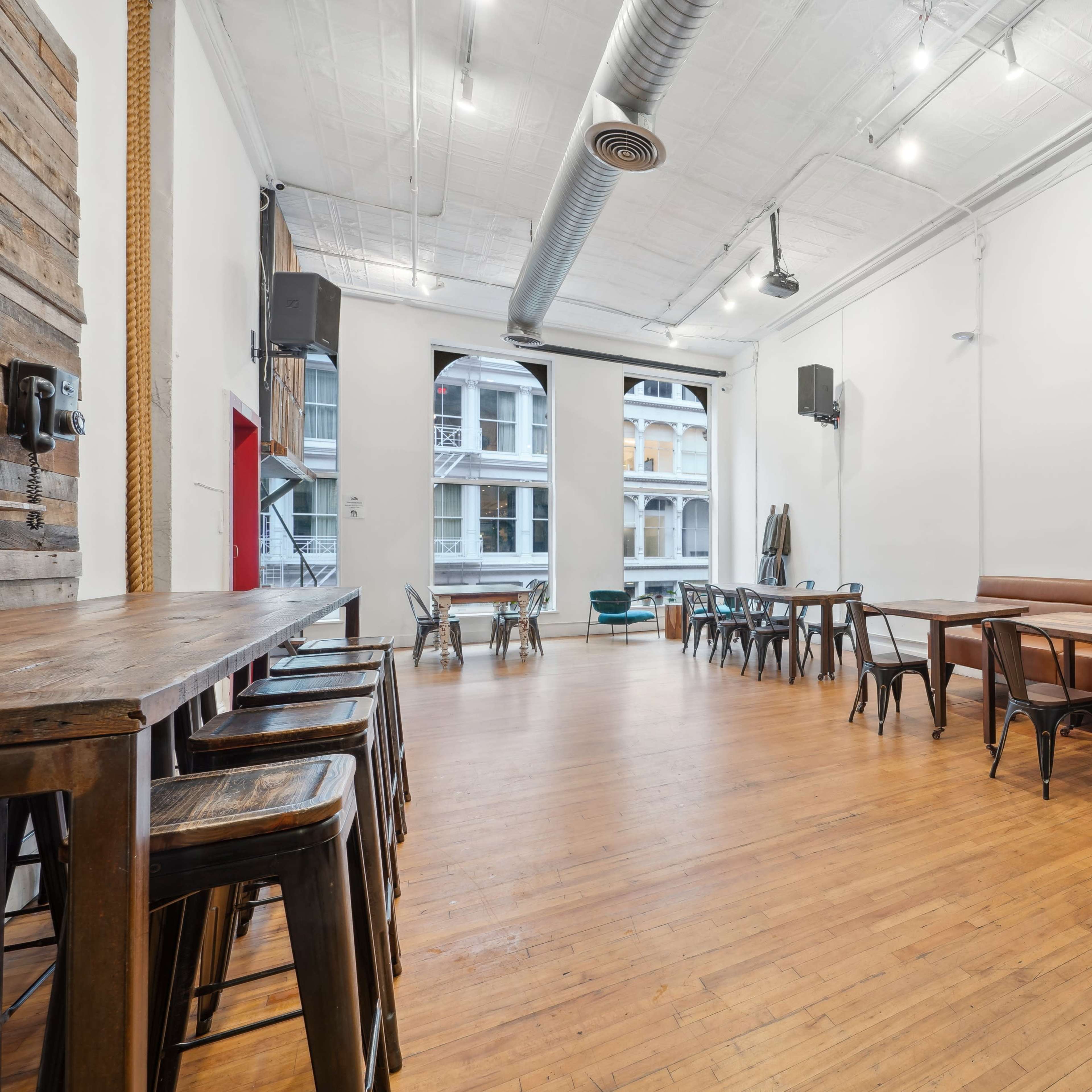 A spacious empty interior of a cafe or restaurant with wooden tables, metal stools, and a long leather bench along the wall.