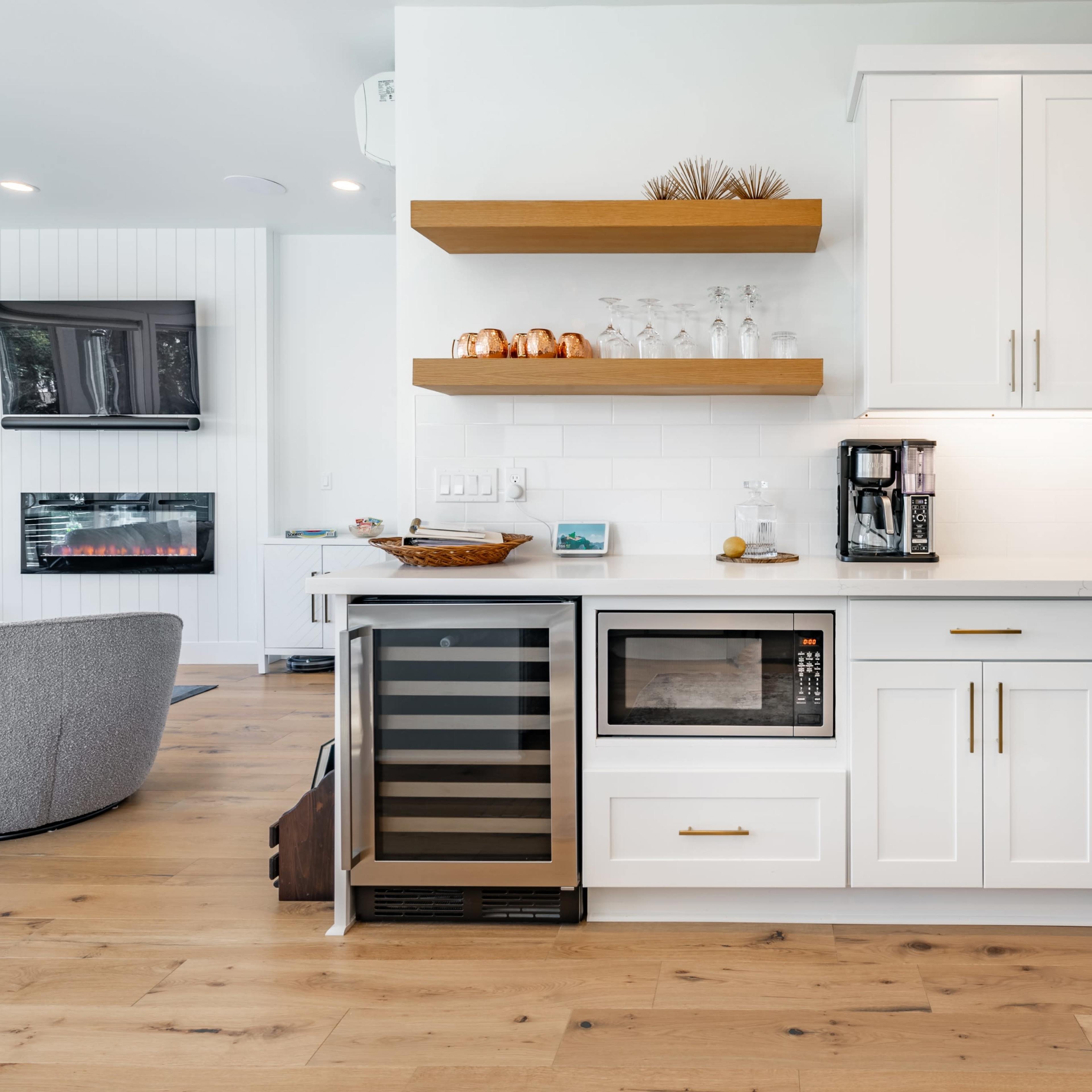 A modern kitchen features white cabinets, open wooden shelves, a stainless steel refrigerator, and a built-in microwave.