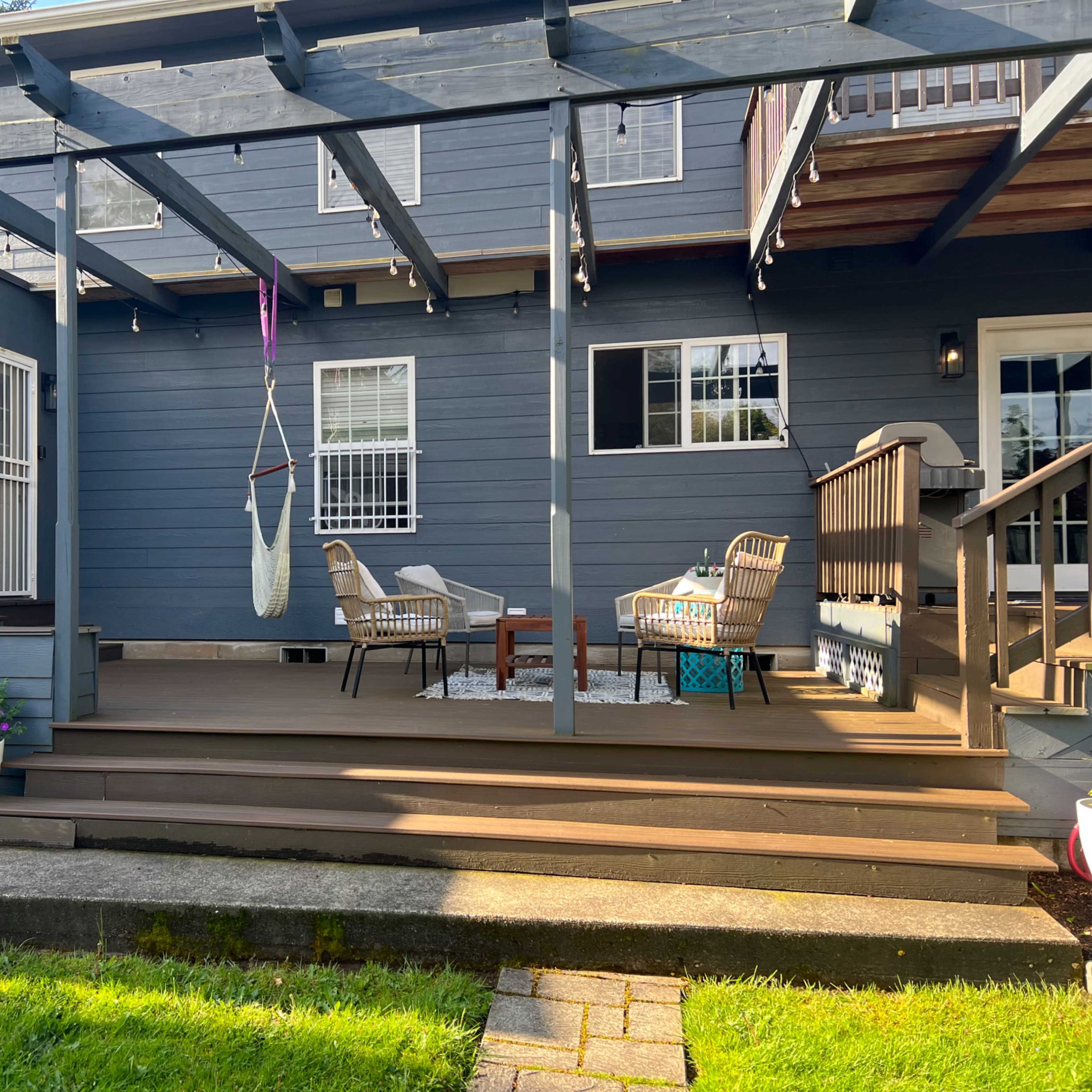 The scene shows a wooden deck with outdoor seating, a hammock, and a large window displaying the word "POOL," all set against a blue house.