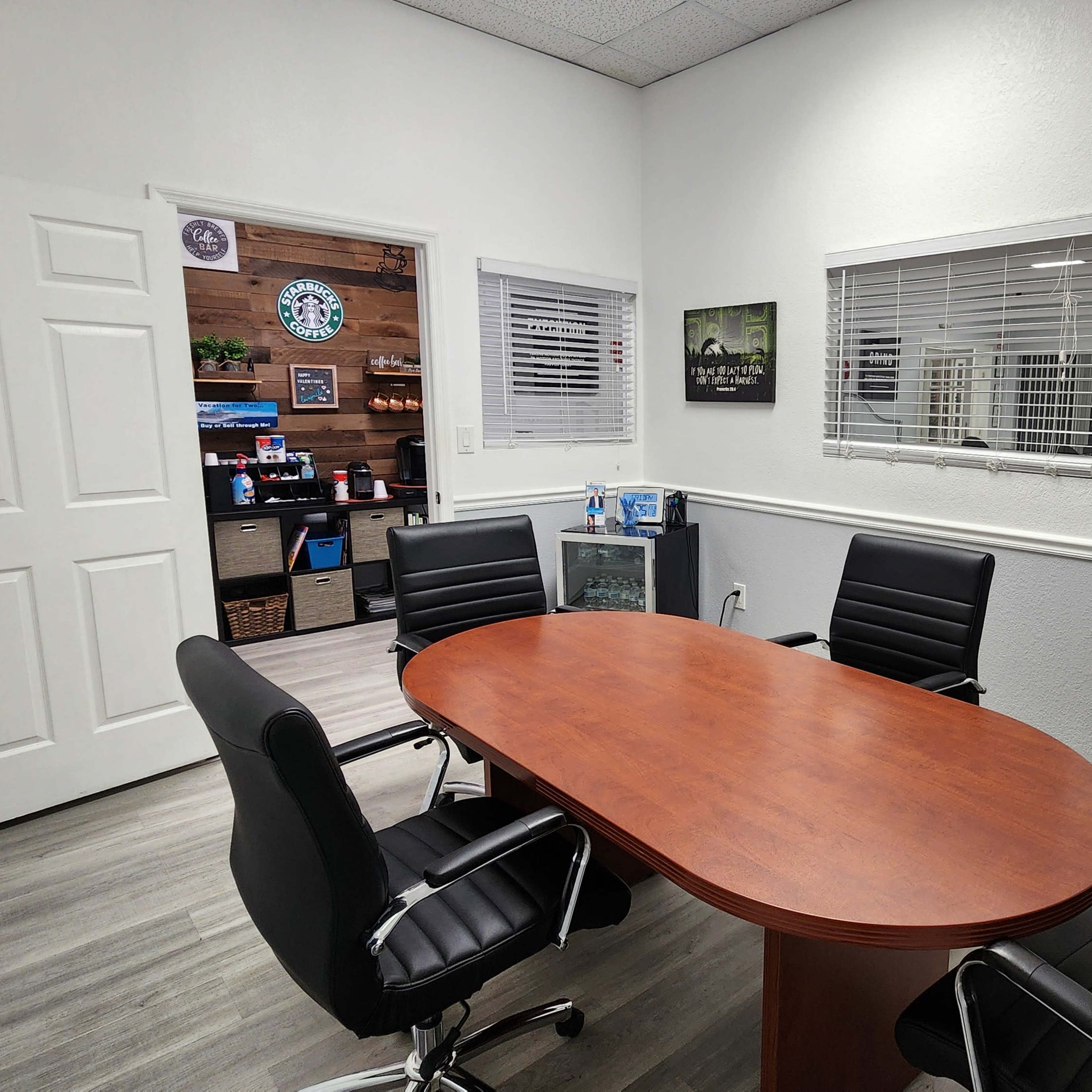 A conference room with a wooden oval table surrounded by four black chairs and a door leading to another room.