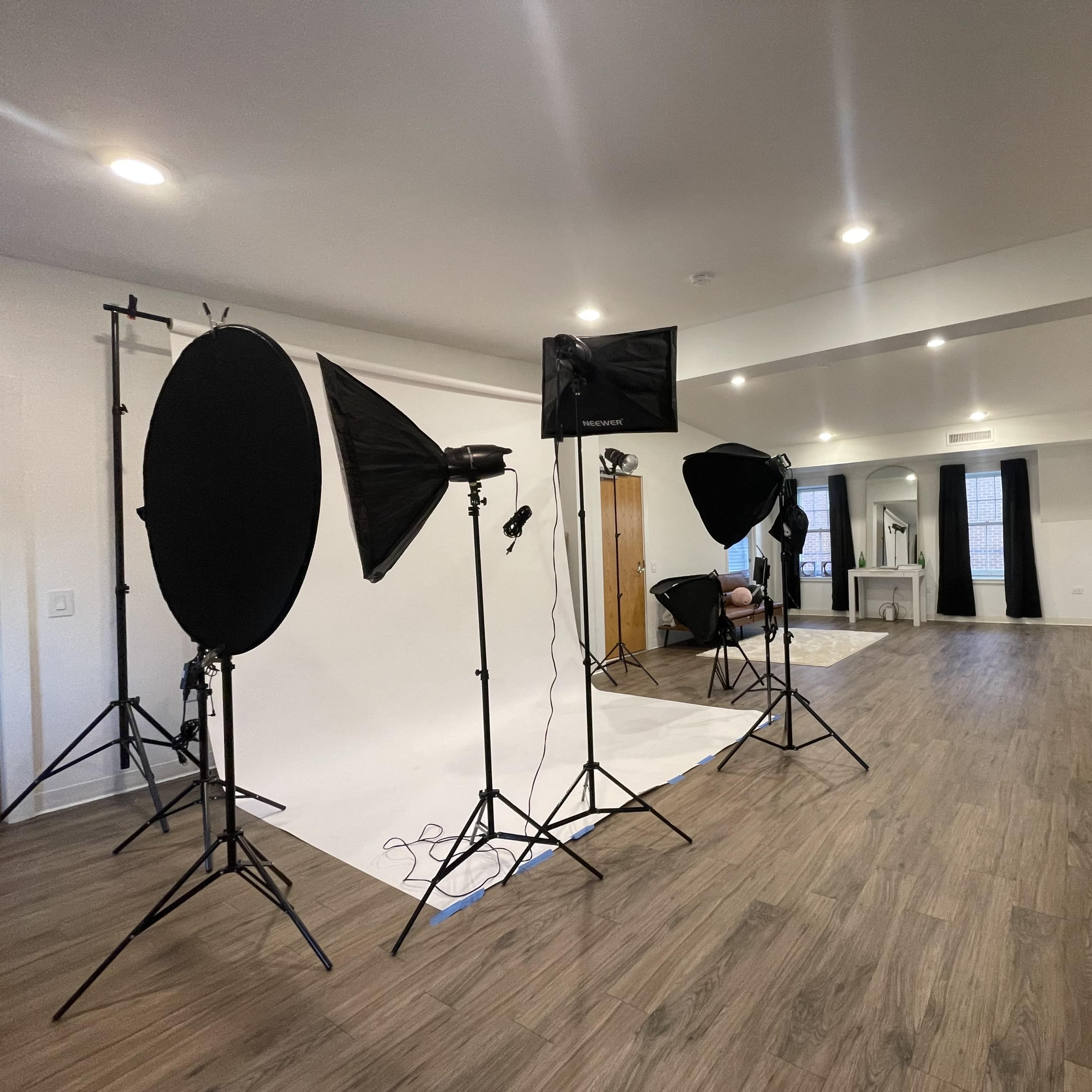 A photography studio setup in a spacious room, featuring several lighting equipment and a backdrop.