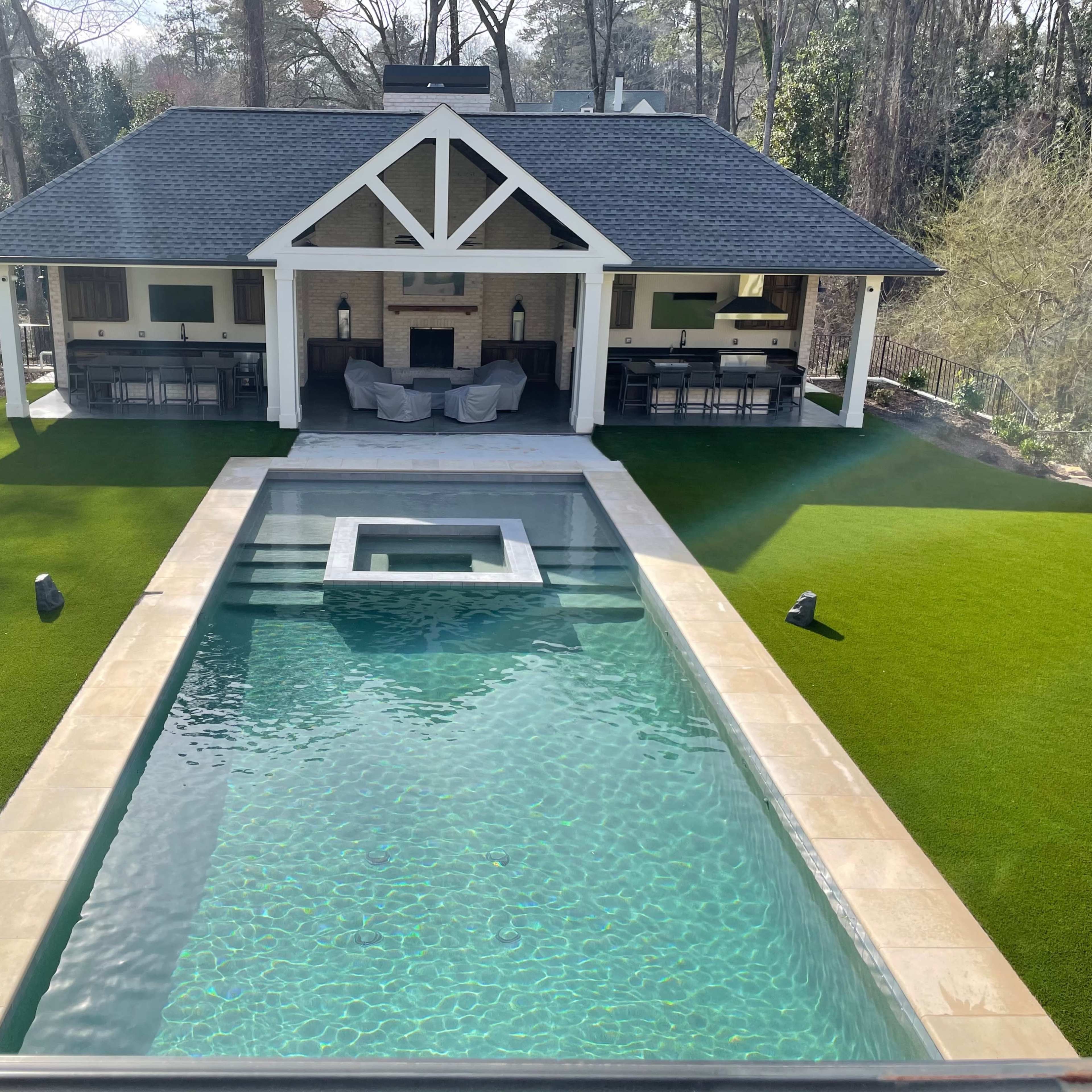 A modern house overlooking a rectangular swimming pool with a spa, surrounded by artificial grass and a putting green.