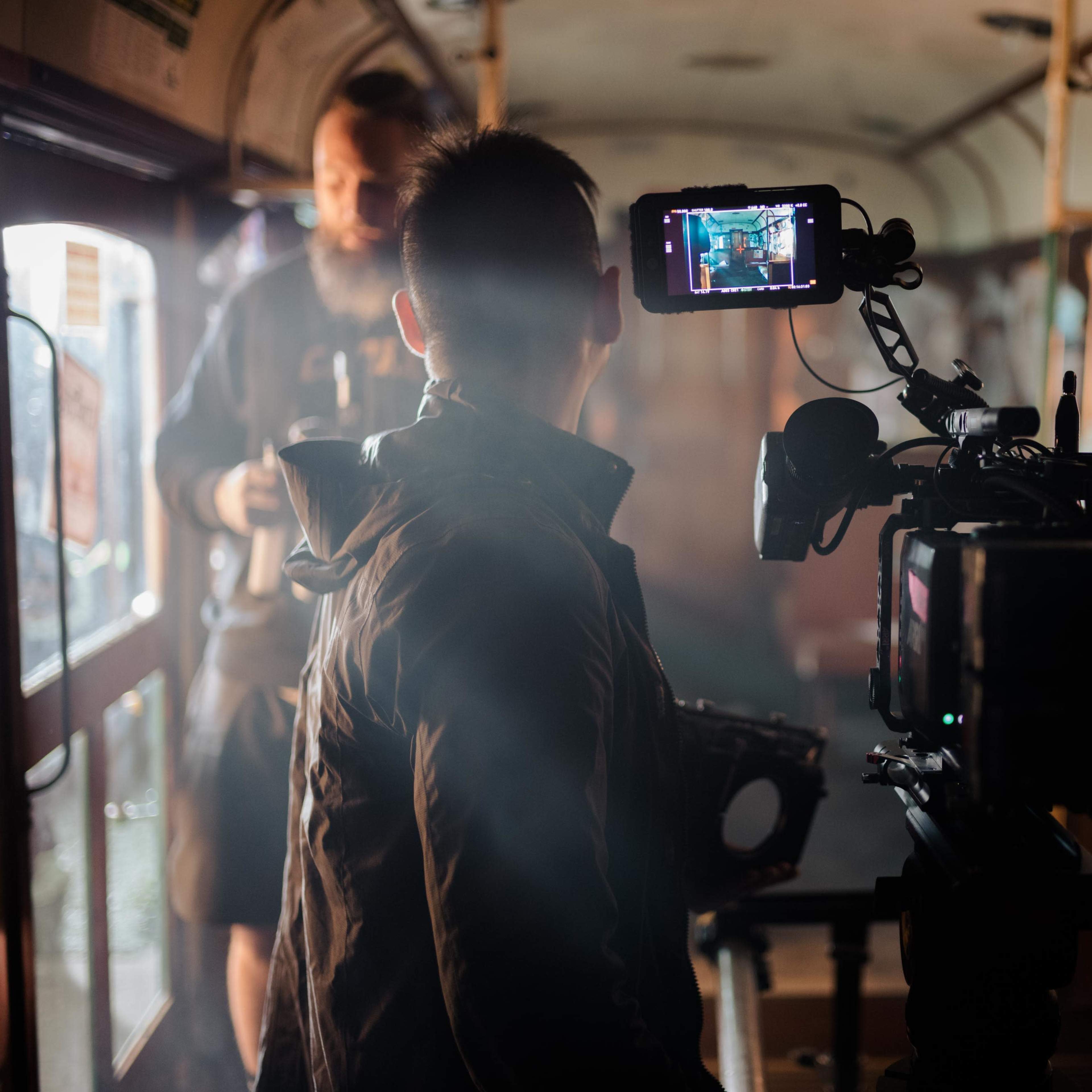 A camera operator records a scene inside an old train carriage, surrounded by smoke and crew members.