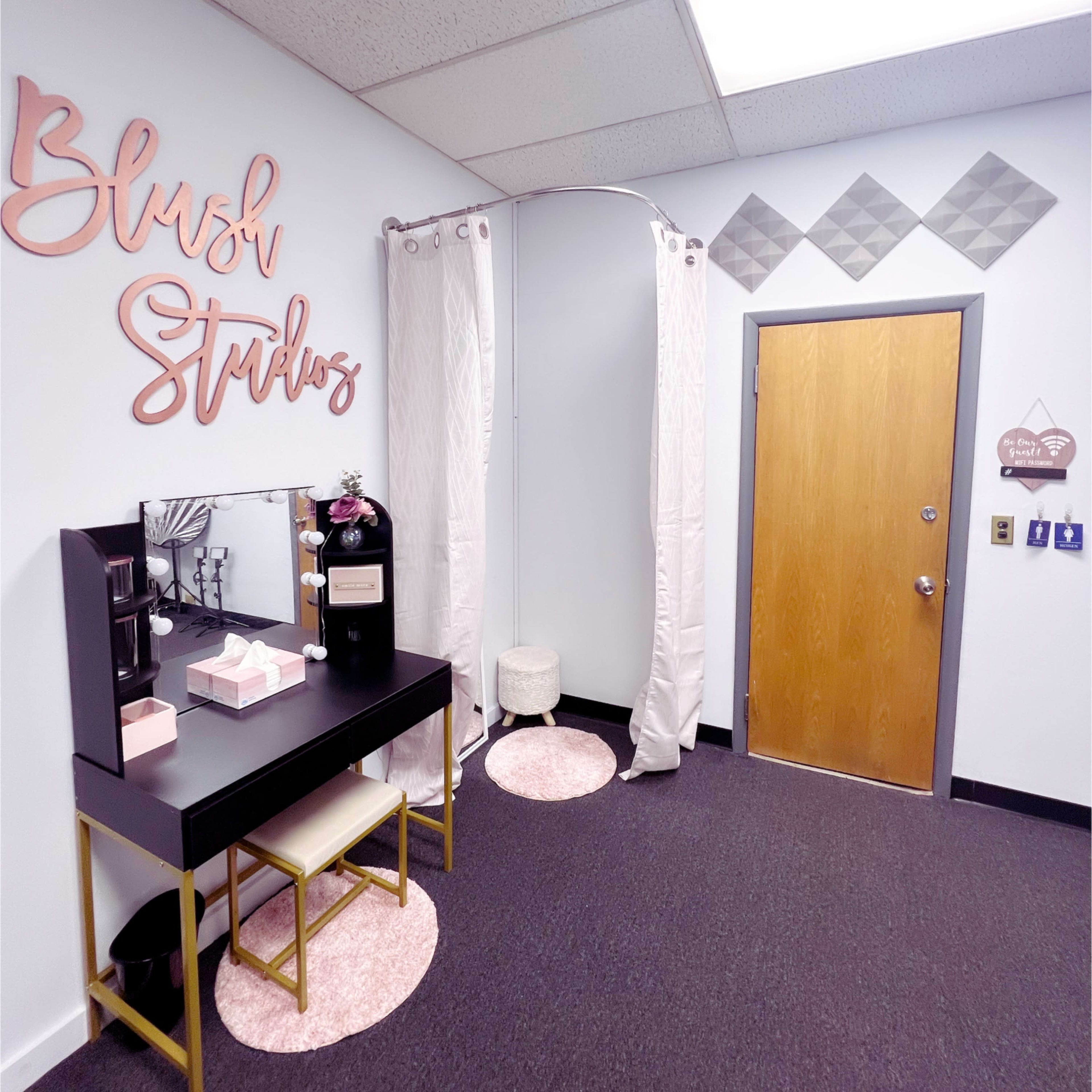 A neat beauty studio entrance featuring a black vanity table with mirror, pink accents, and a door with a decorative sign.