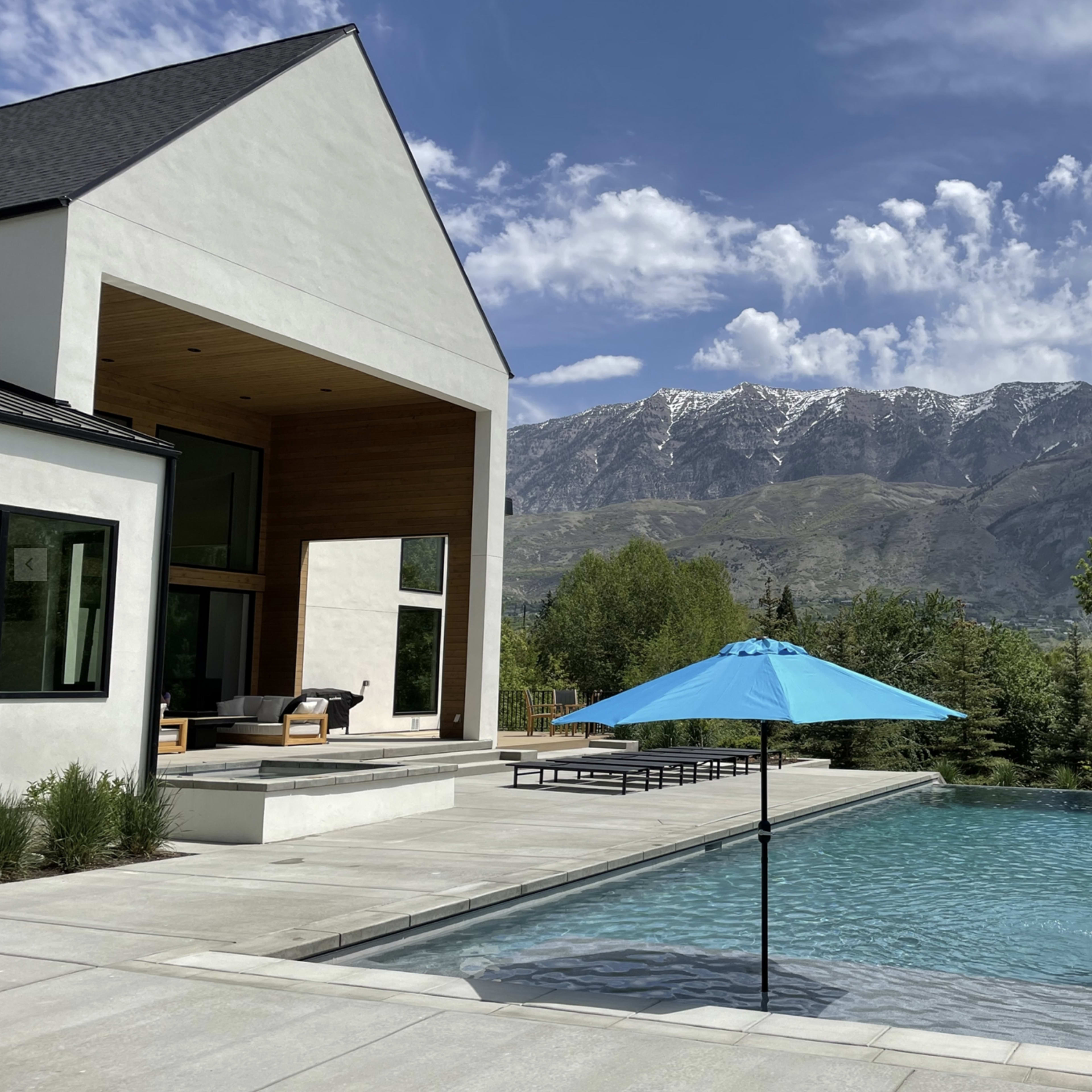 A modern house with a spacious patio overlooks a swimming pool and mountains in the background.