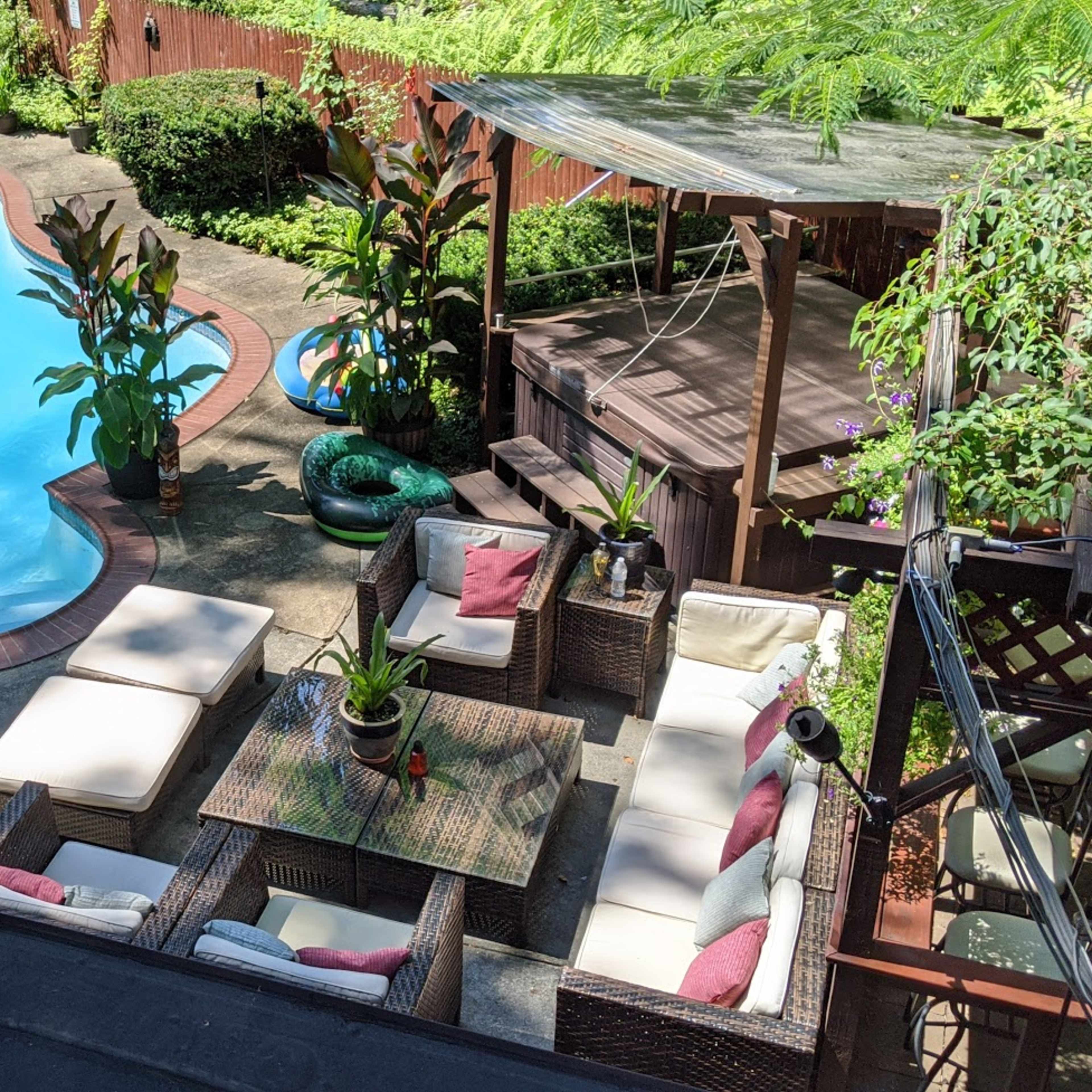 A backyard with a swimming pool surrounded by lounge furniture, potted plants, and a gazebo.