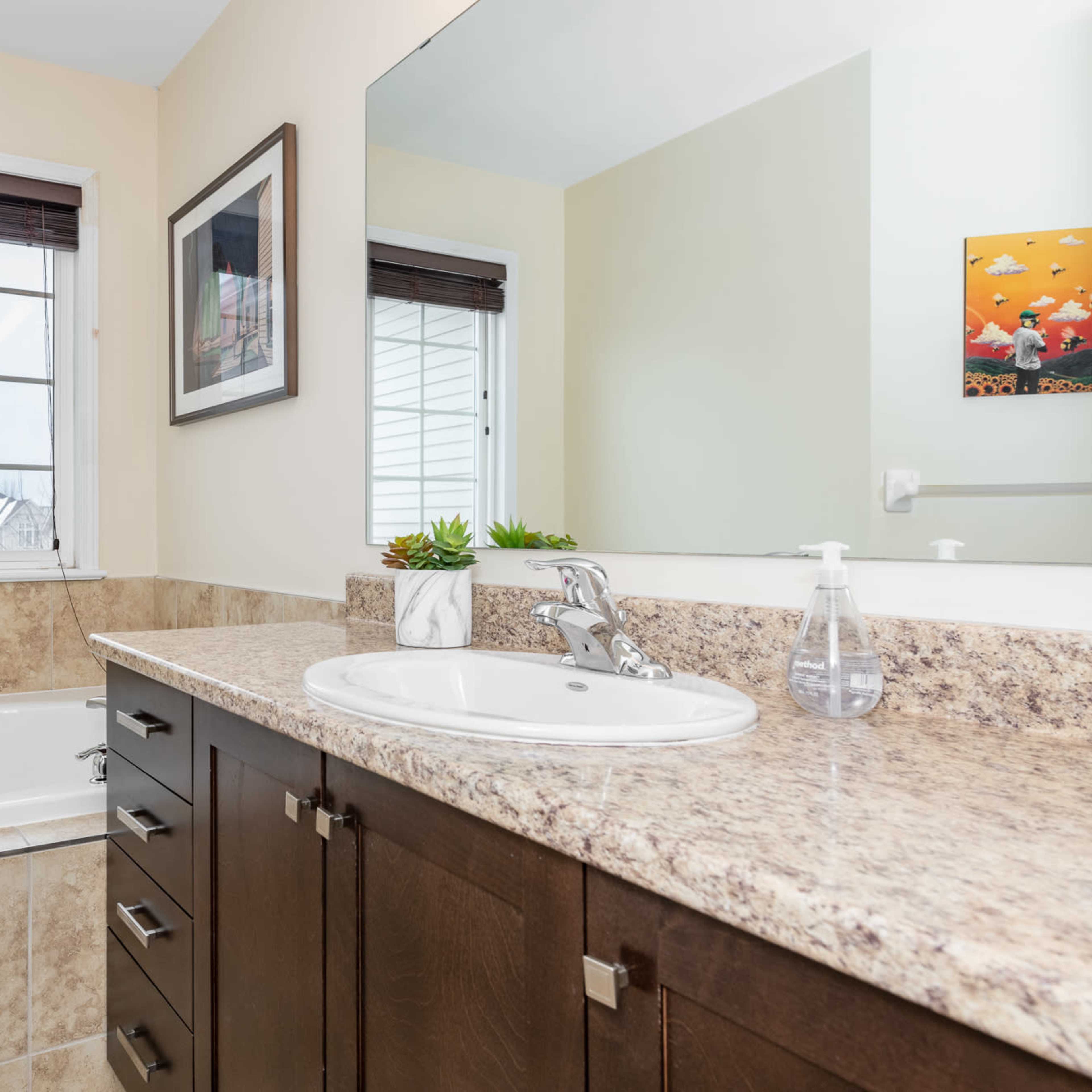 A bathroom featuring a bathtub beside a window, a sink with a granite countertop, and wooden cabinetry.