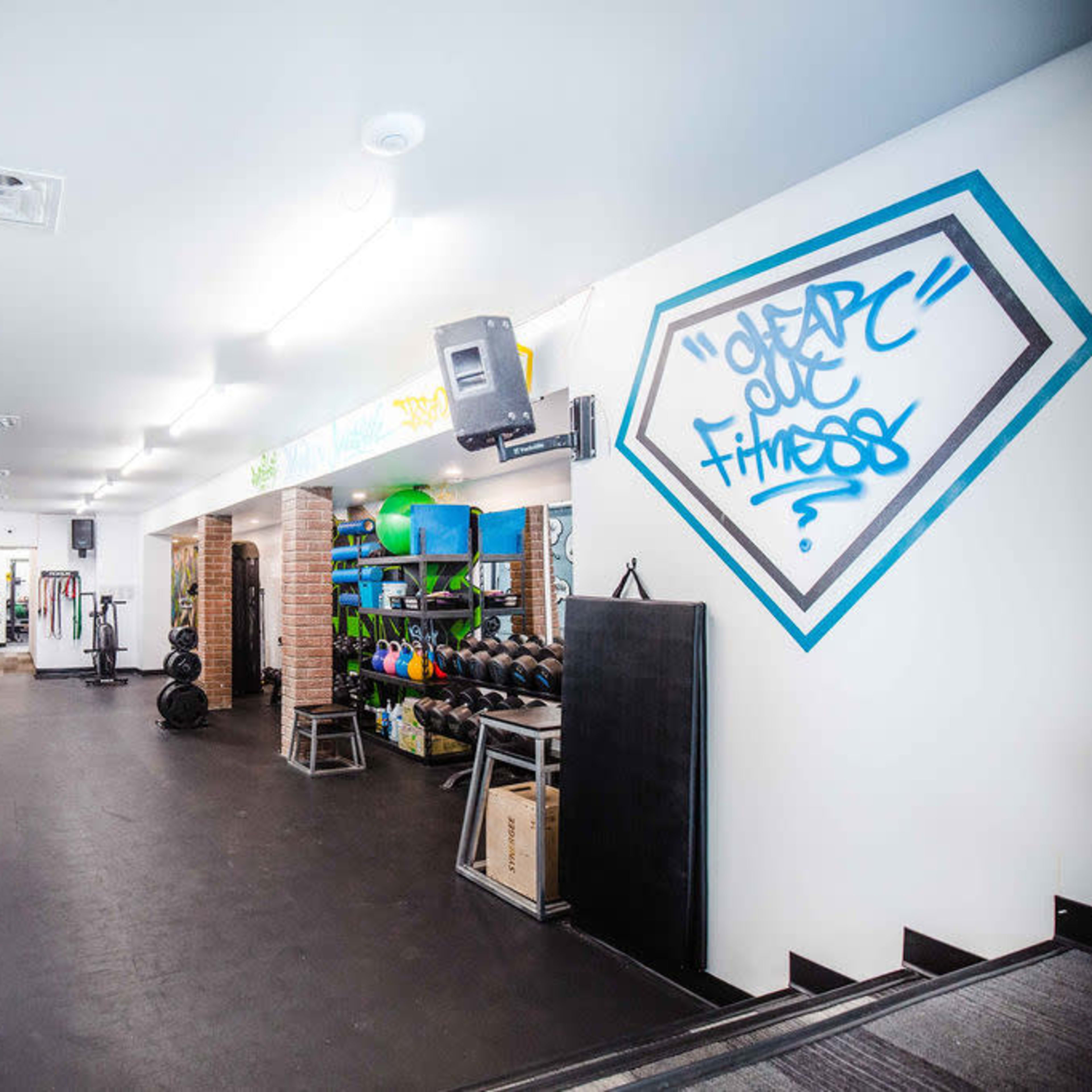 A gym interior featuring weightlifting equipment, a wall adorned with graffiti, and neatly organized fitness gear on shelves.