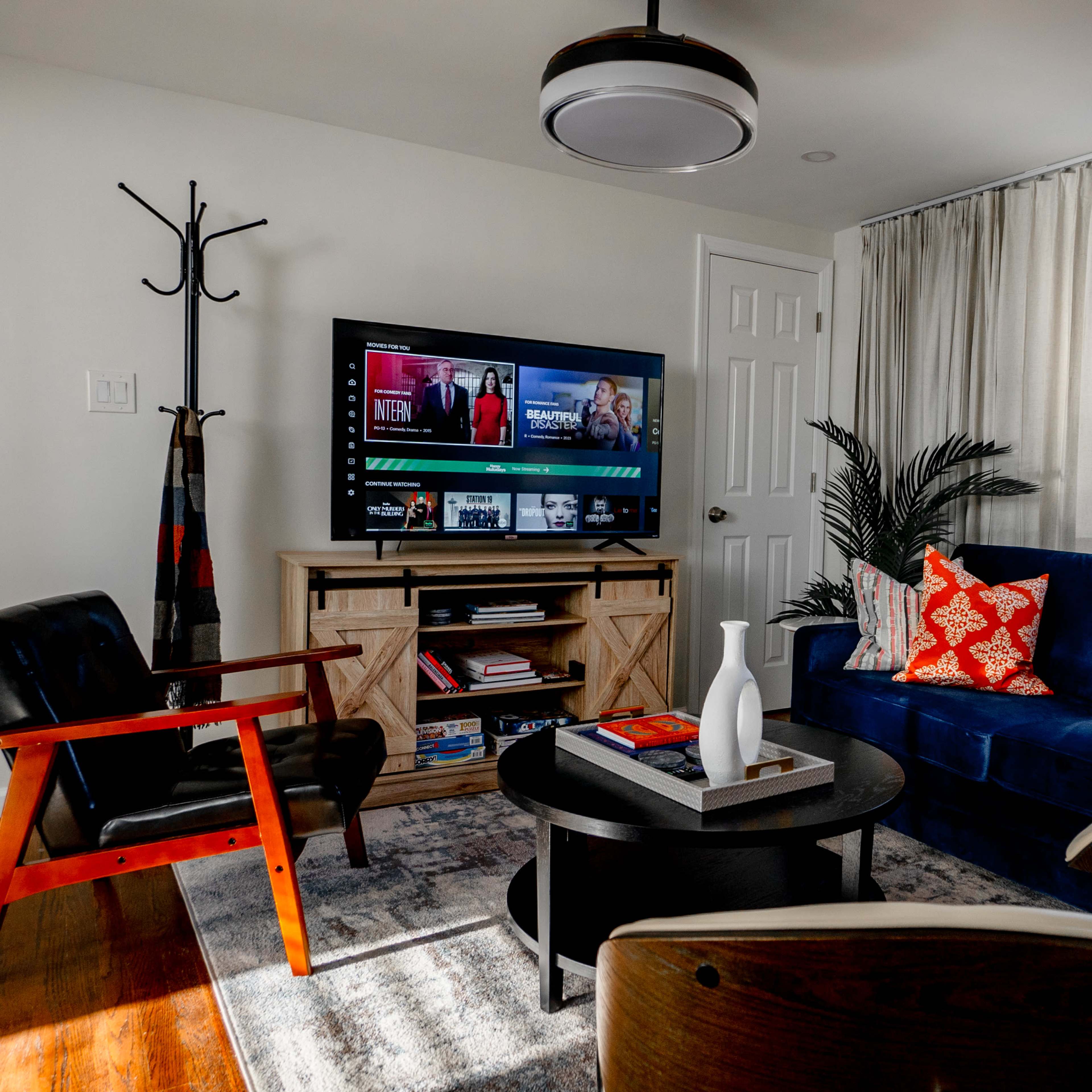 A living room with a blue sofa, a round coffee table, a wooden entertainment center with a television, and various decorative pillows on the sofa.