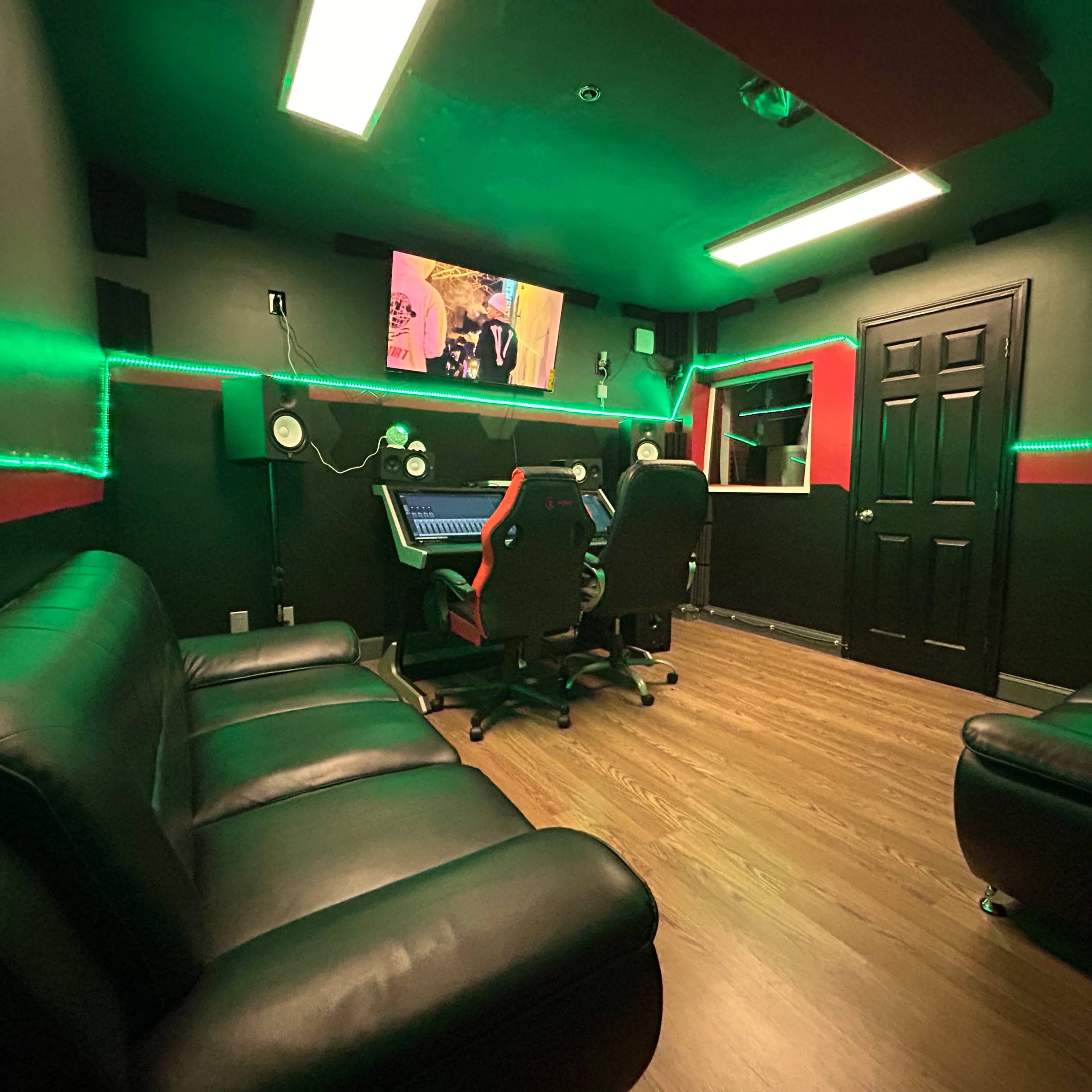 A recording studio with two black leather sofas, a mixing console, and green LED lights illuminating the walls.
