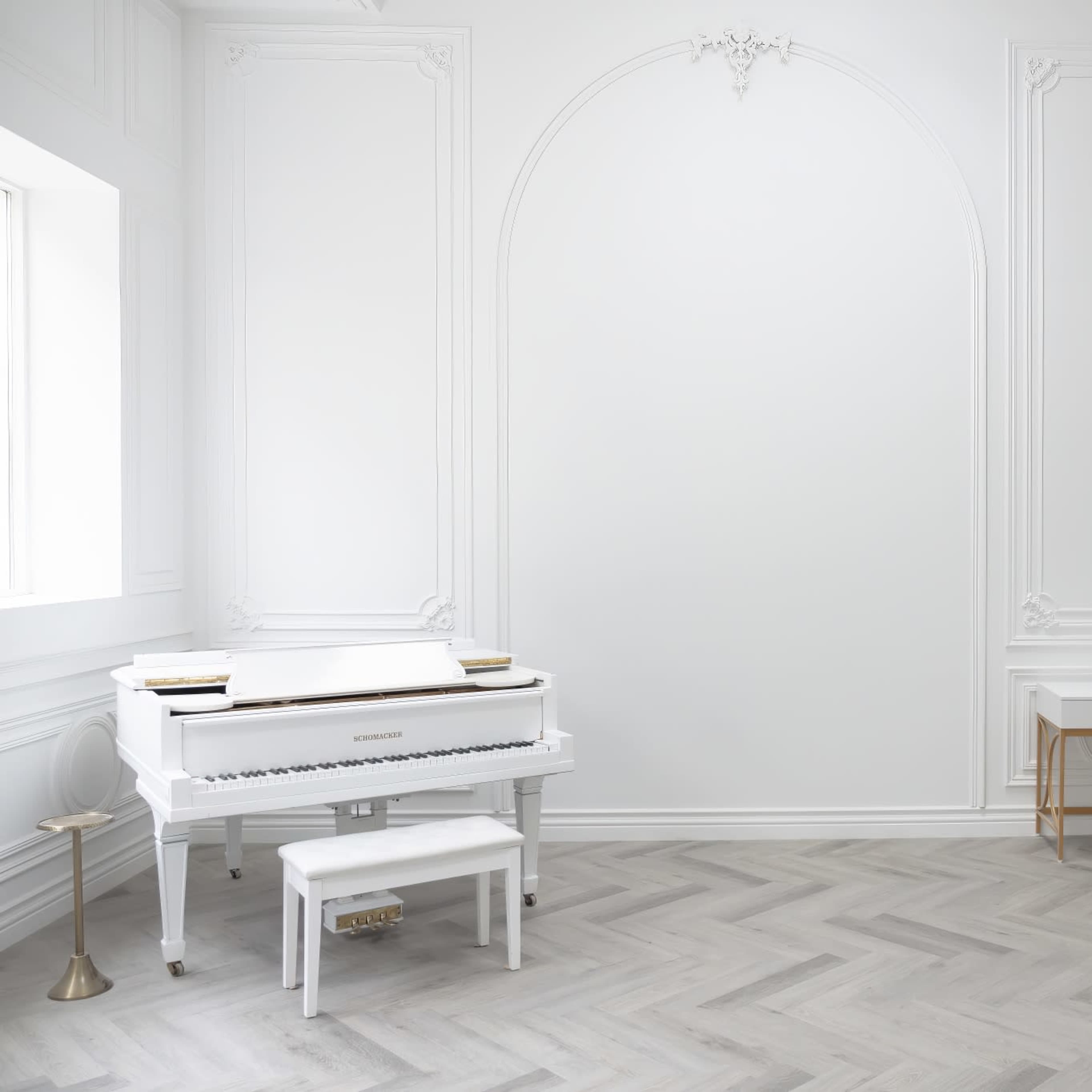 The room features a white grand piano, a modern desk, and a cream-colored chair against a light-colored, intricately designed wall.