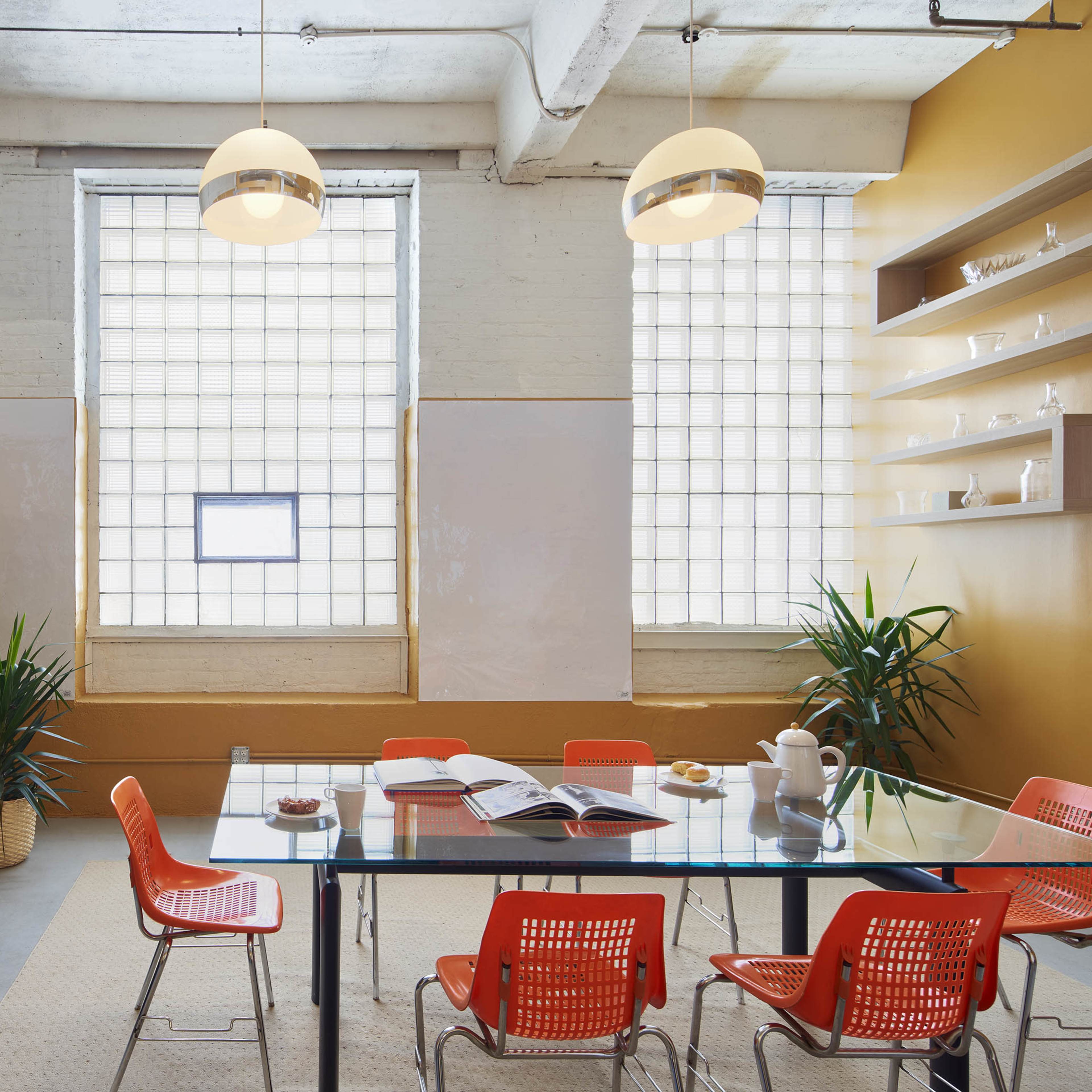 A spacious open-plan office featuring wooden tables, modern pendant lighting, and colorful wall art.