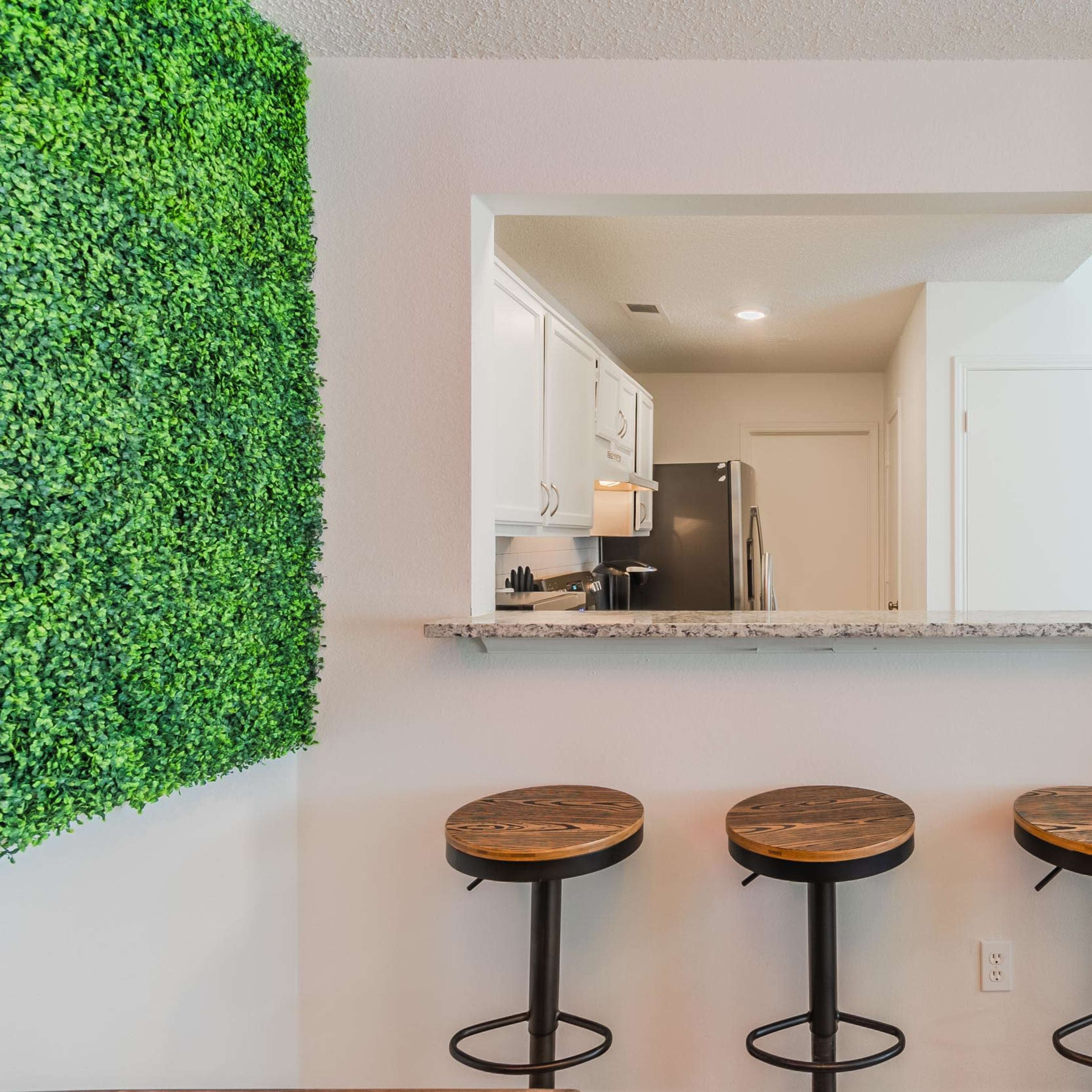 A kitchen area with a granite countertop and three wooden bar stools in front of a small opening to the kitchen.