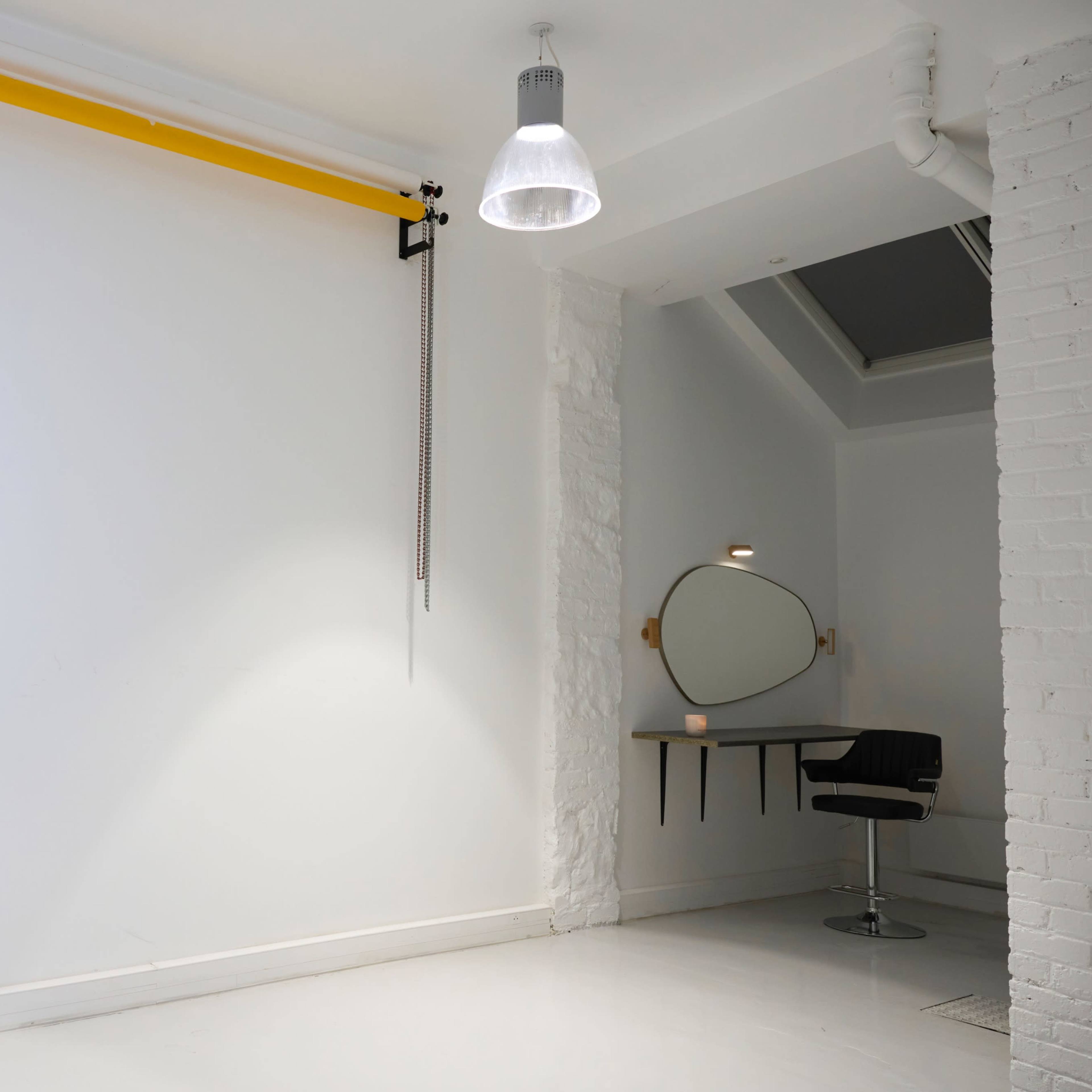 A minimalist interior space with a white wall, a black chair positioned near a circular mirror, and a yellow bar mounted on the wall.